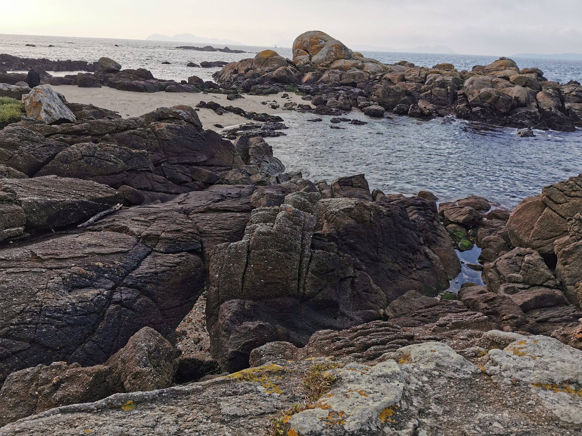 Costa rocosa de granito junto a una pequeña playa y el mar bajo cielo nublado.