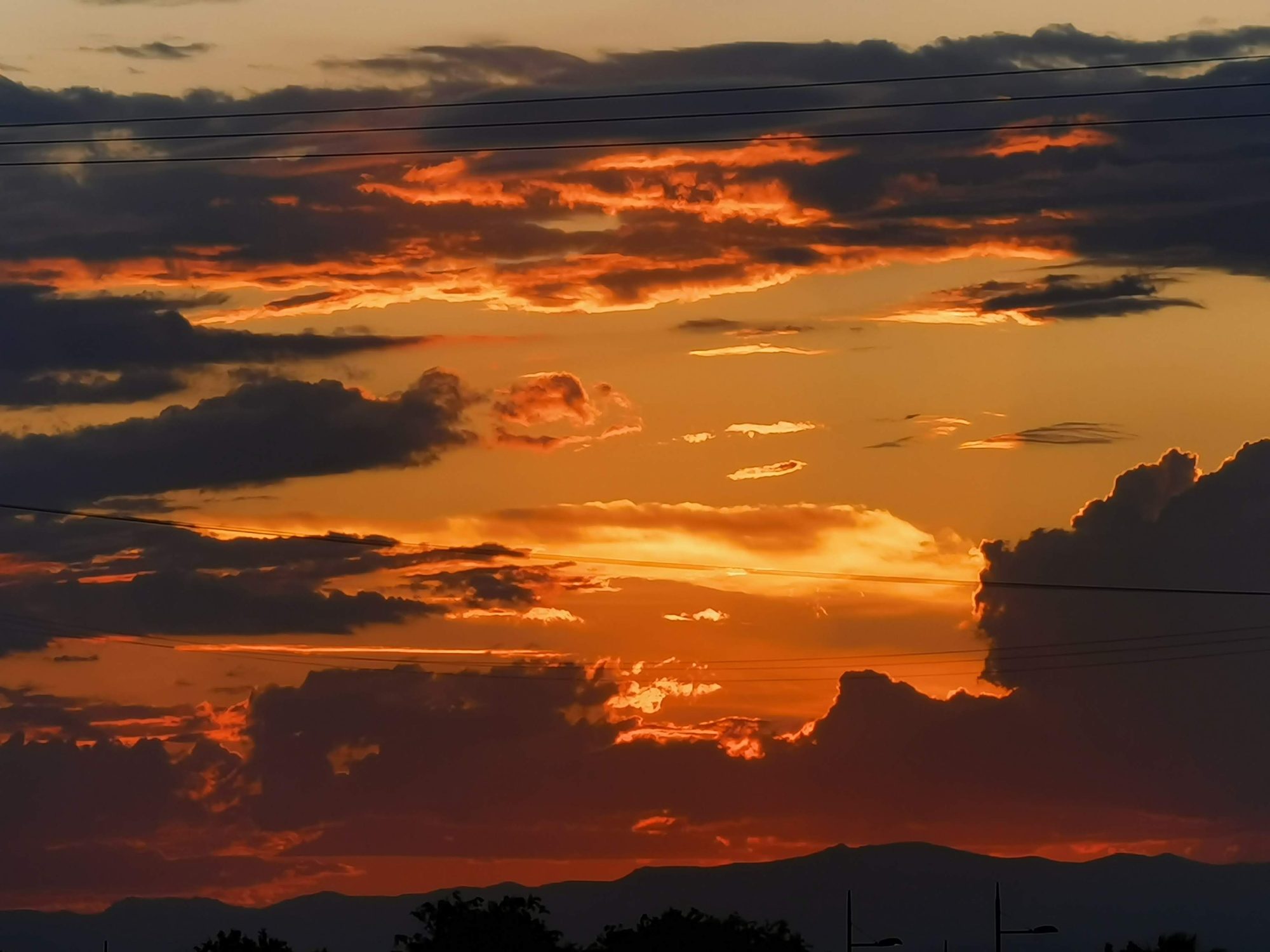Cielo de atardecer con nubes oscuras iluminadas por tonos naranjas y dorados sobre montañas.