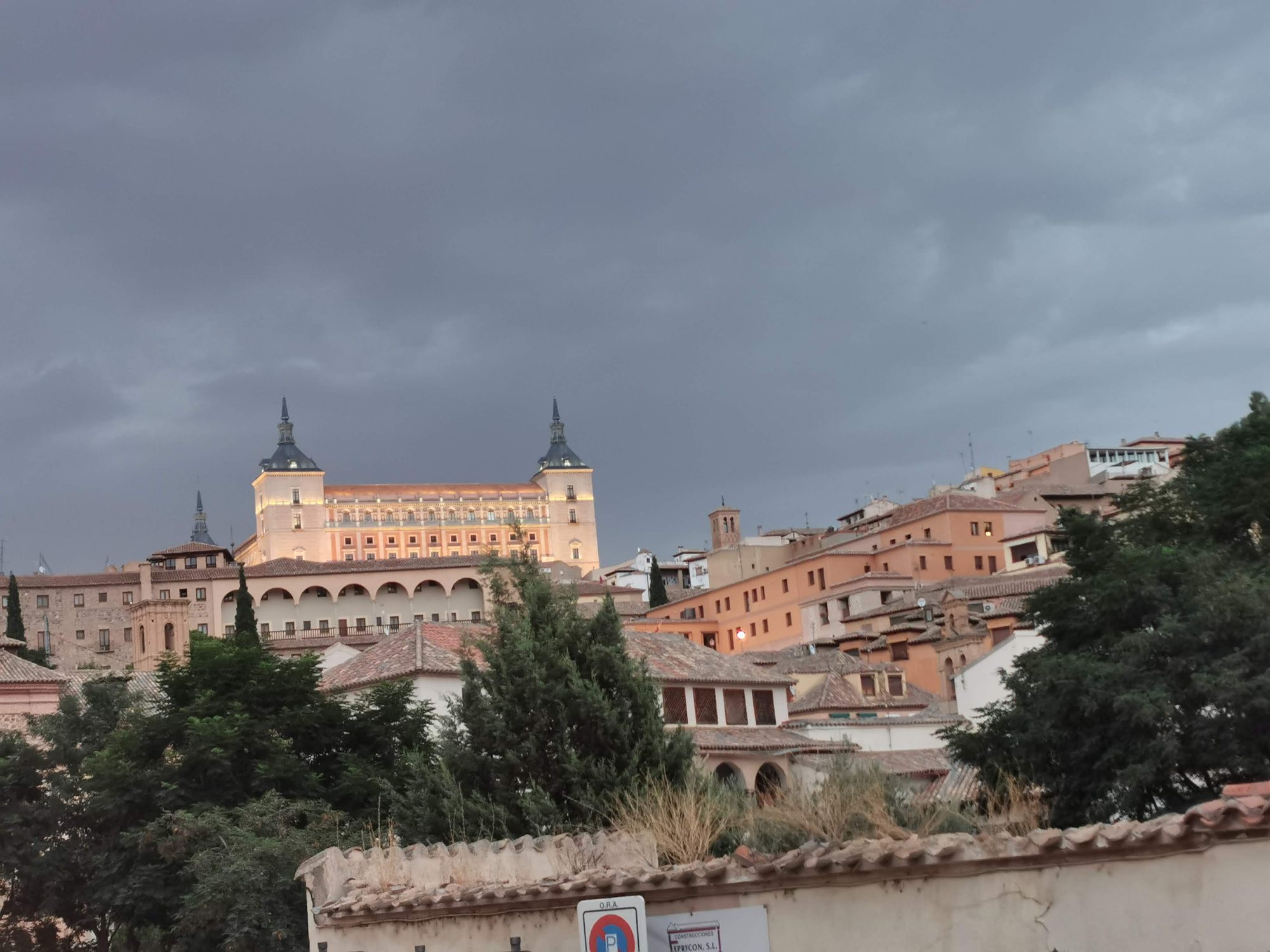 Vista del Alcázar de Toledo iluminado sobre tejados tradicionales bajo un cielo oscuro de tormenta.