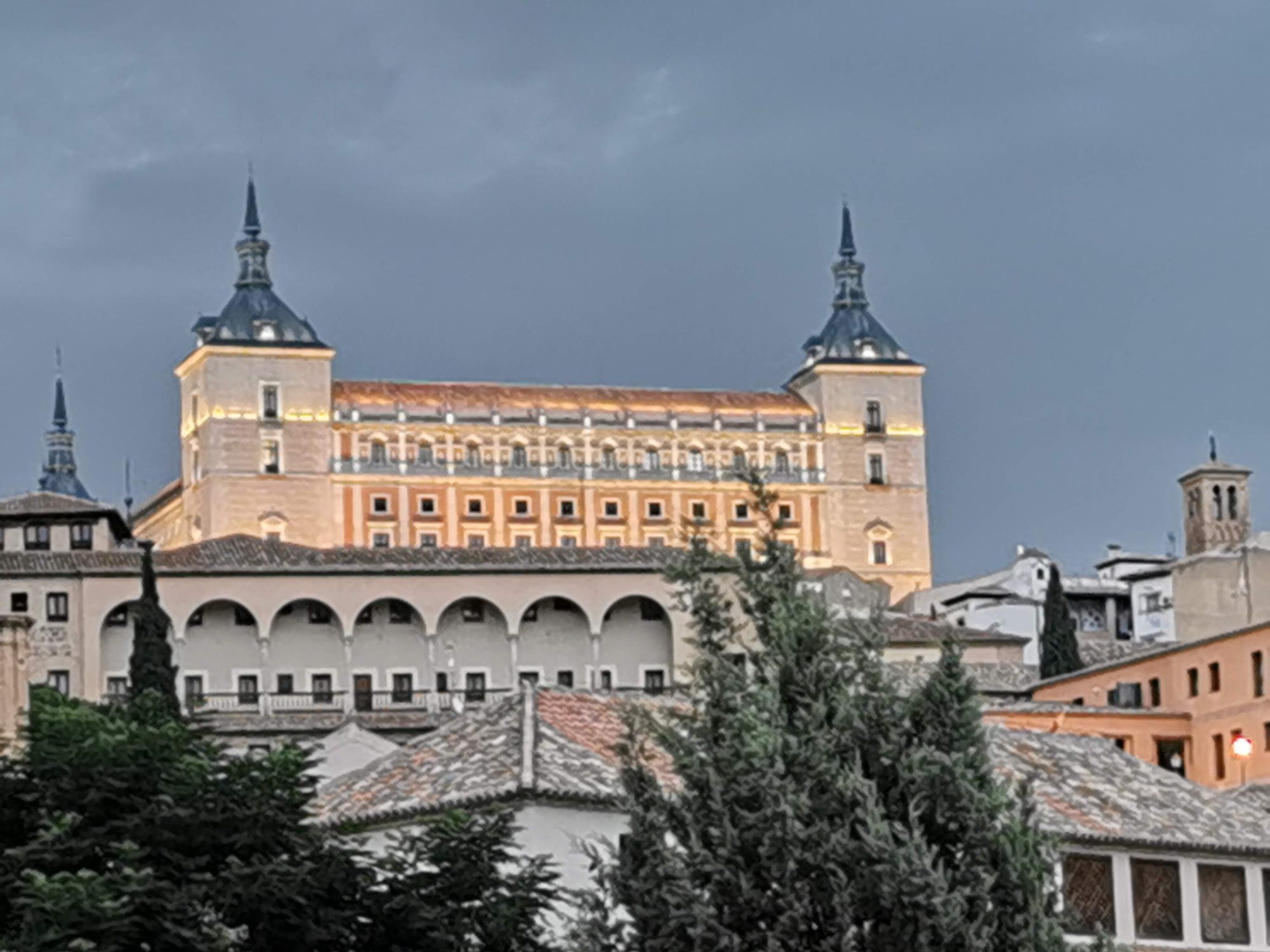 El Alcázar de Toledo iluminado al atardecer sobre los tejados y arcos históricos.
