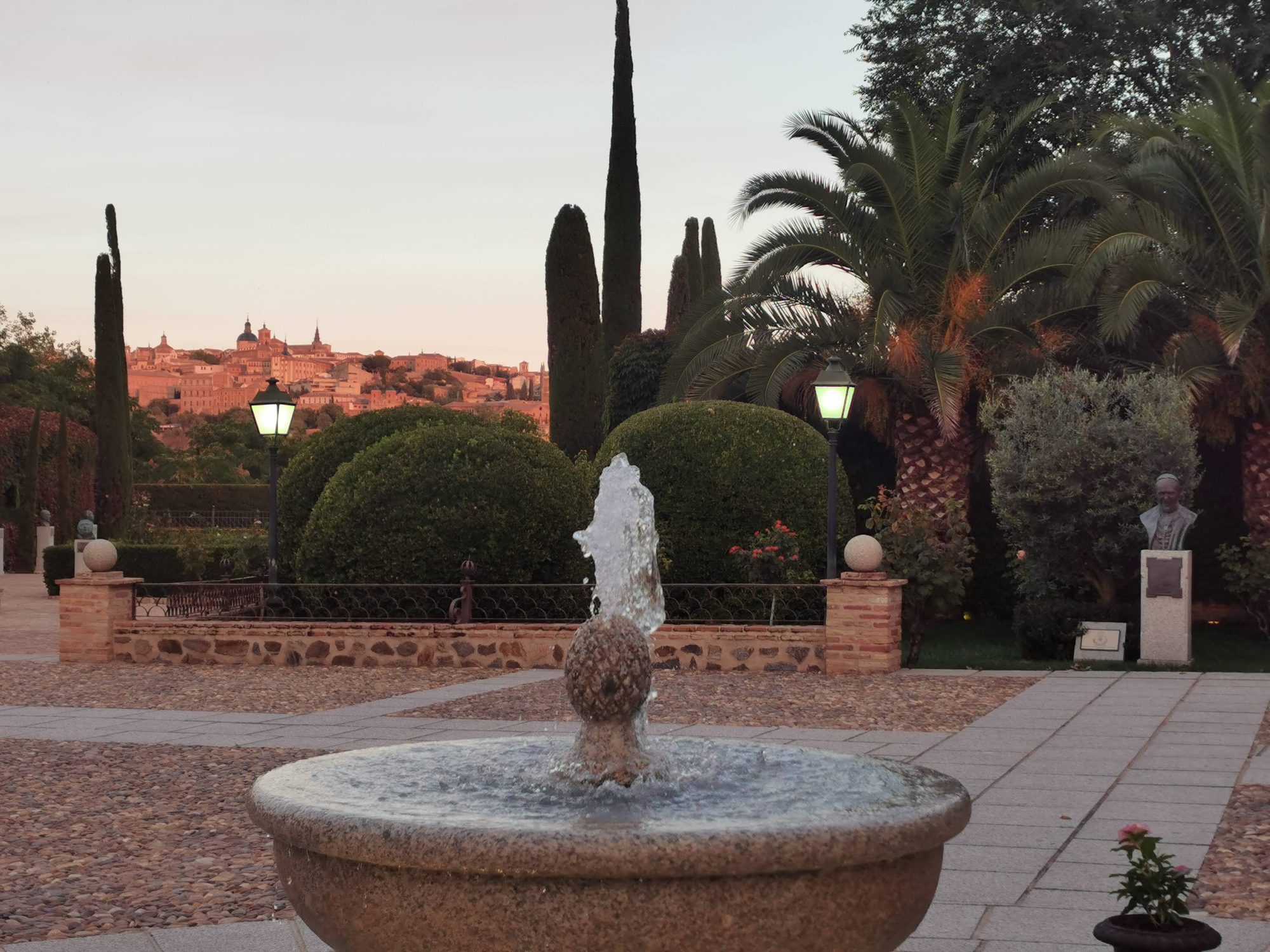 Fuente de piedra en un jardín con la panorámica de Toledo al atardecer al fondo.