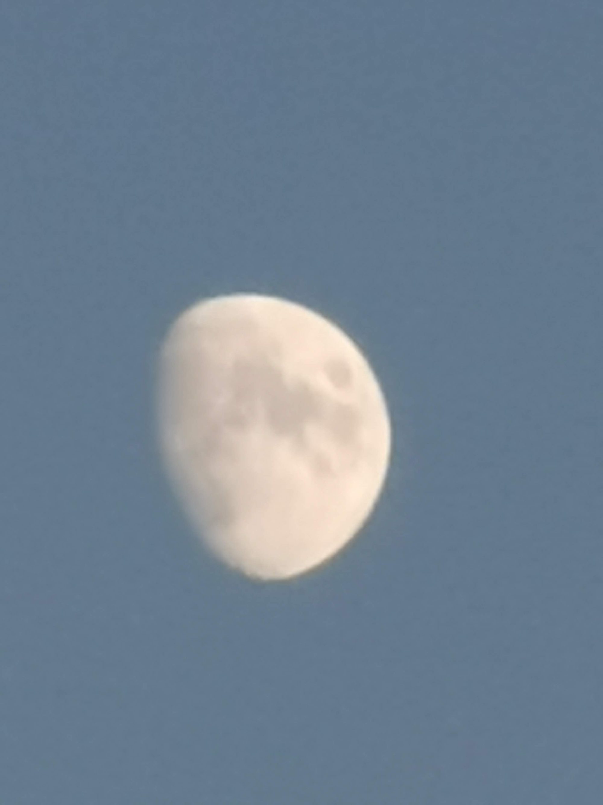 Luna gibosa creciente visible sobre un cielo azul diurno despejado.