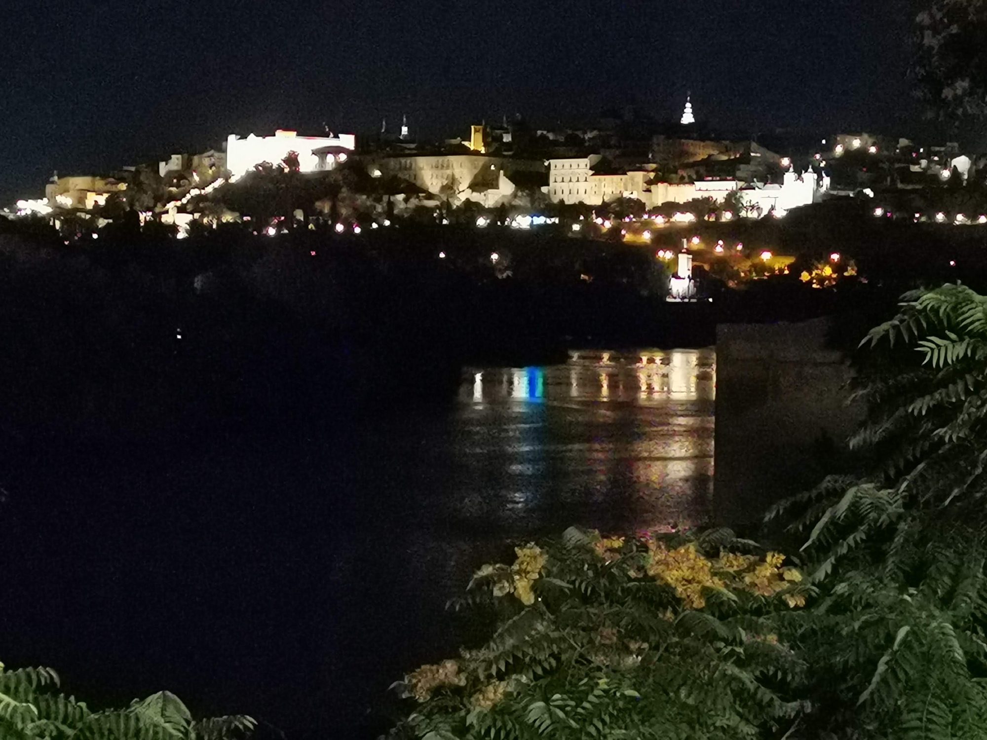 Vista nocturna de Toledo iluminada sobre la colina reflejándose en el río Tajo.