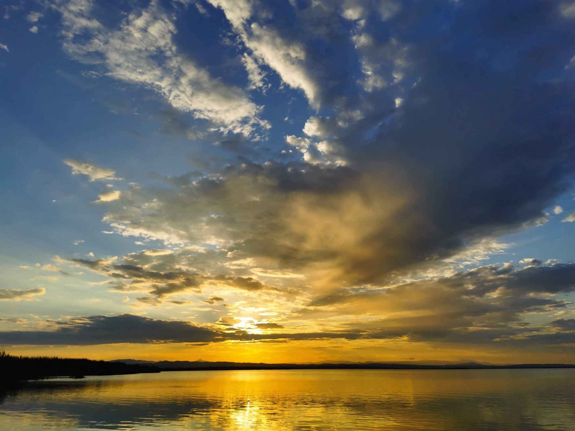 Atardecer dorado sobre aguas tranquilas con nubes iluminadas por los últimos rayos de sol.