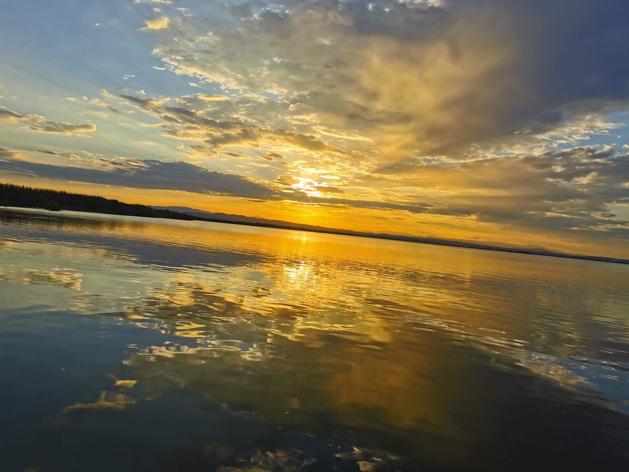 Puesta de sol dorada con nubes reflejándose sobre las aguas calmas de una laguna.