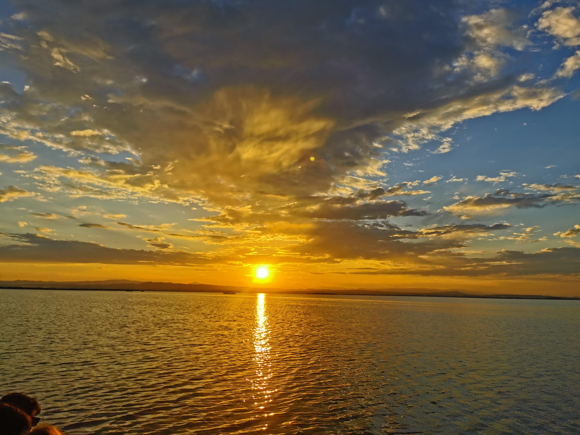 Puesta de sol dorada sobre aguas tranquilas con nubes iluminadas en el horizonte.