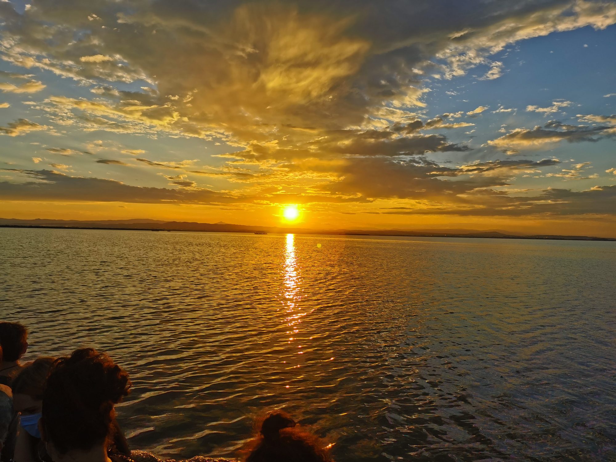Puesta de sol dorada sobre el agua con nubes iluminadas en el horizonte.