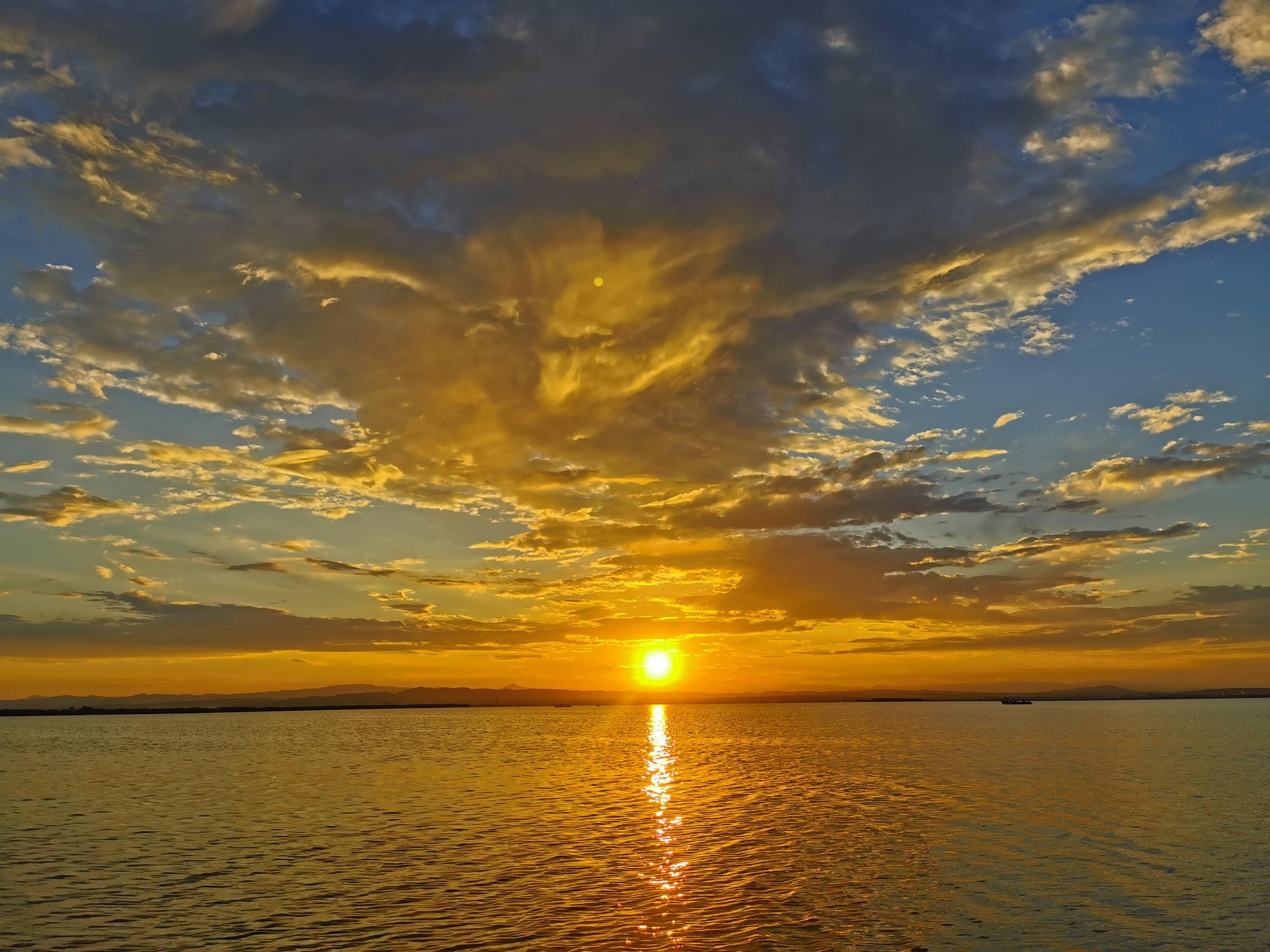 Puesta de sol dorada sobre el agua con nubes iluminadas en el horizonte.
