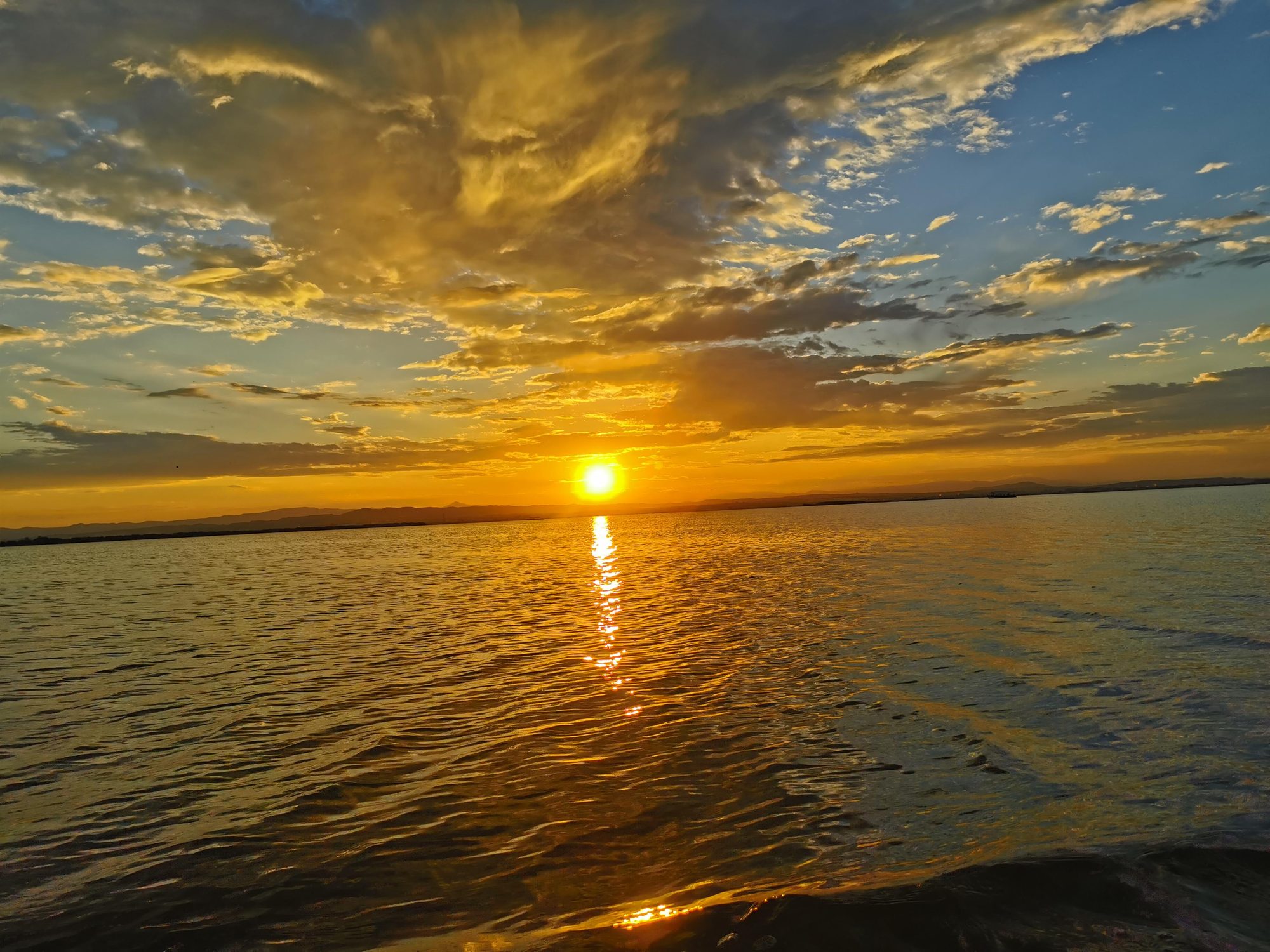 Puesta de sol dorada reflejándose en el agua bajo un cielo con nubes iluminadas.