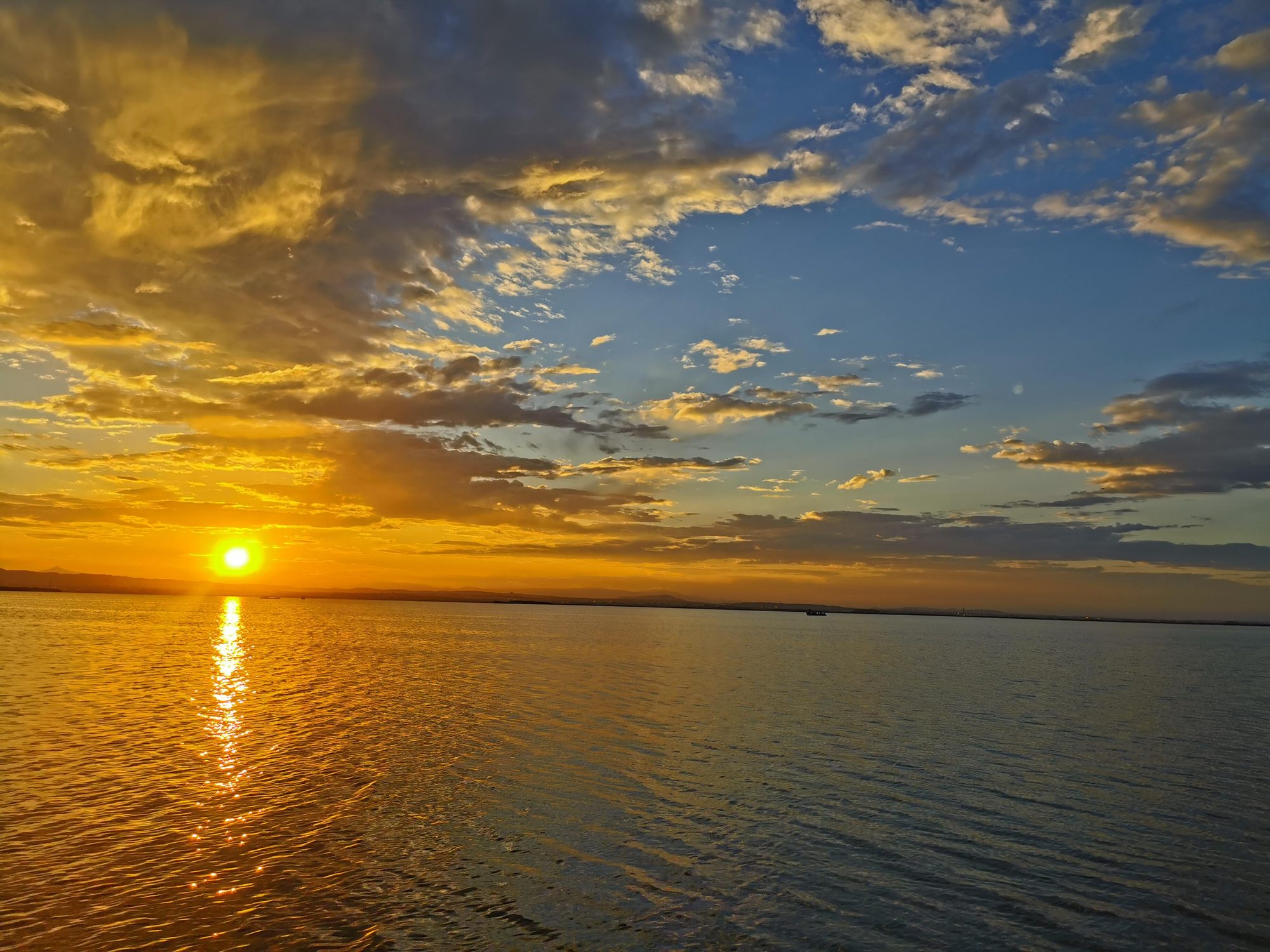 Atardecer dorado reflejado sobre el agua tranquila con nubes dispersas en el cielo.