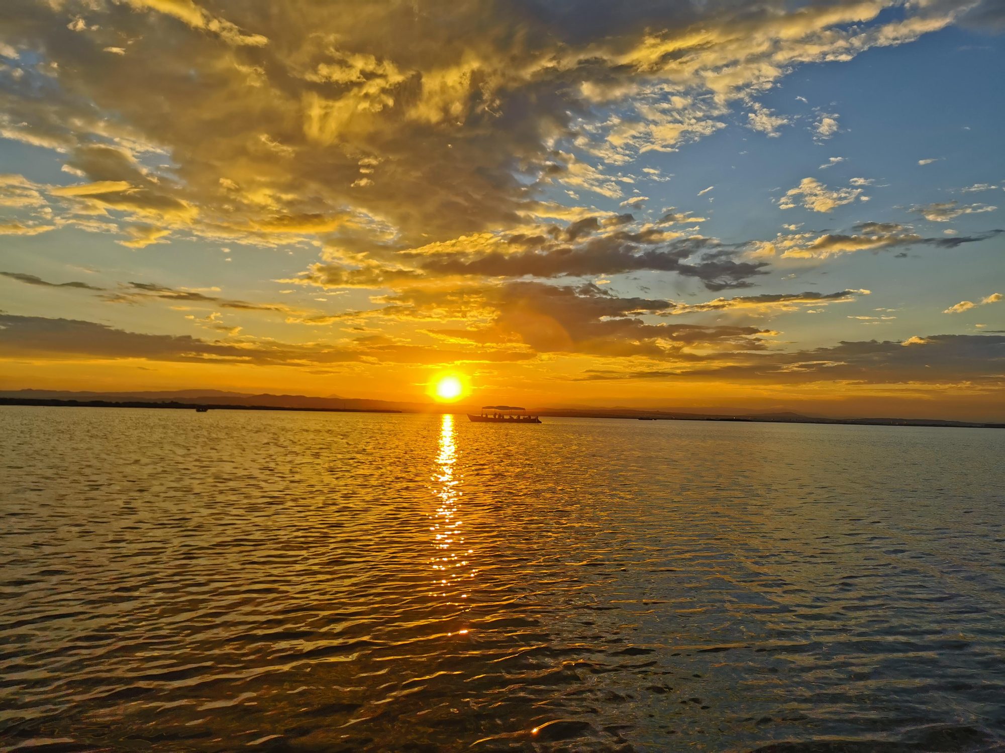 Puesta de sol dorada sobre el agua con una barca navegando en el horizonte.