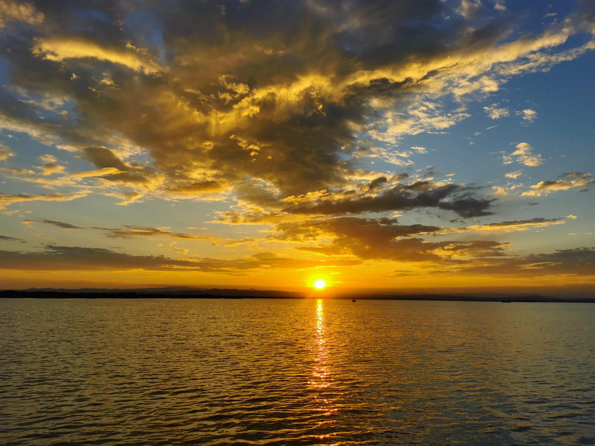 Puesta de sol dorada reflejada sobre el agua con nubes iluminadas al atardecer.