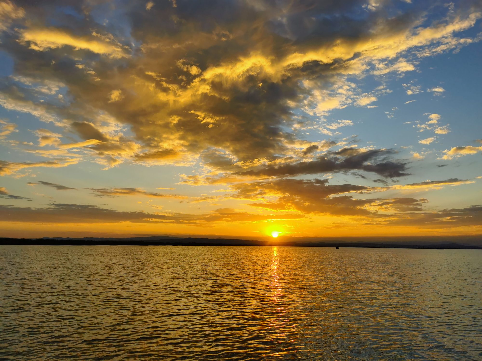 Puesta de sol dorada sobre el agua con nubes iluminadas en el horizonte.