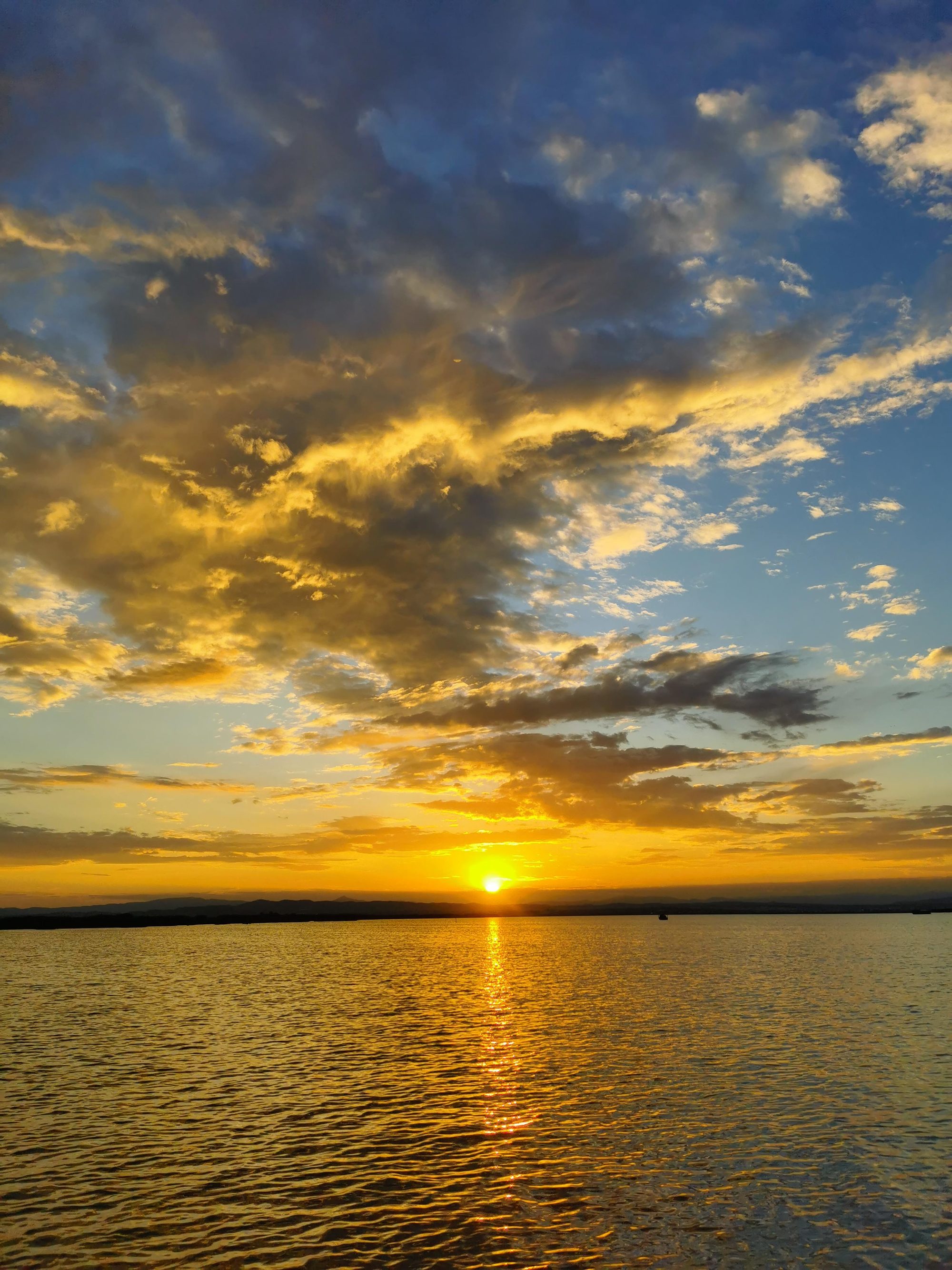 Puesta de sol dorada sobre el agua con nubes iluminadas en el horizonte.