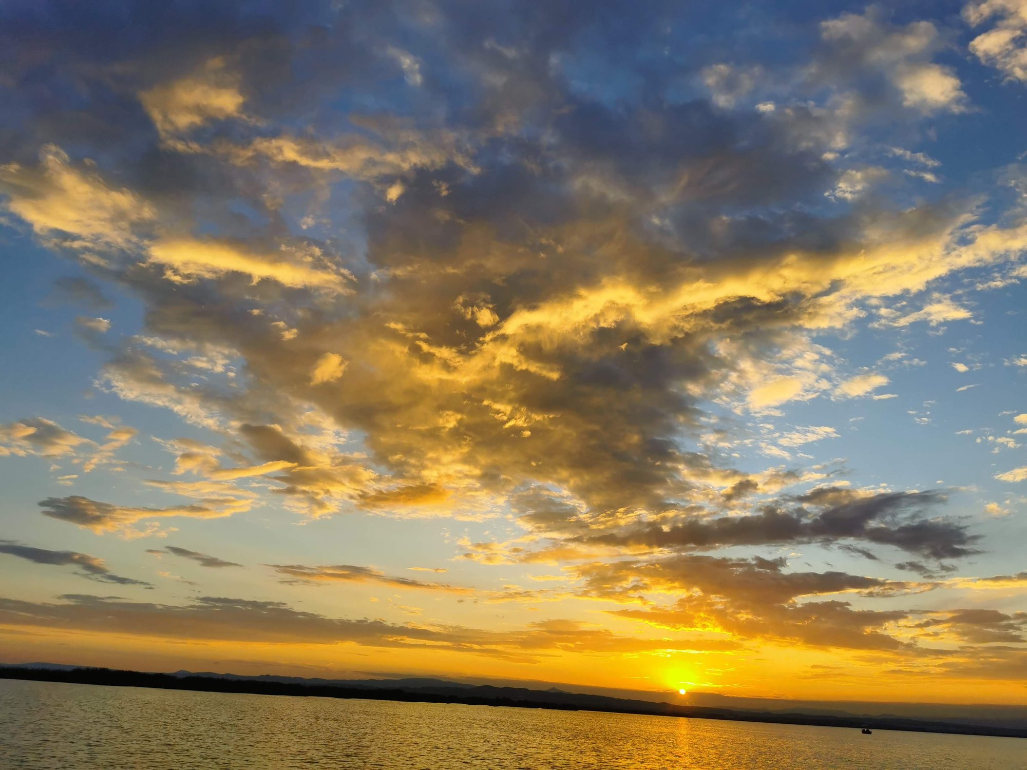 Atardecer dorado sobre aguas tranquilas con nubes iluminadas por el sol poniente.
