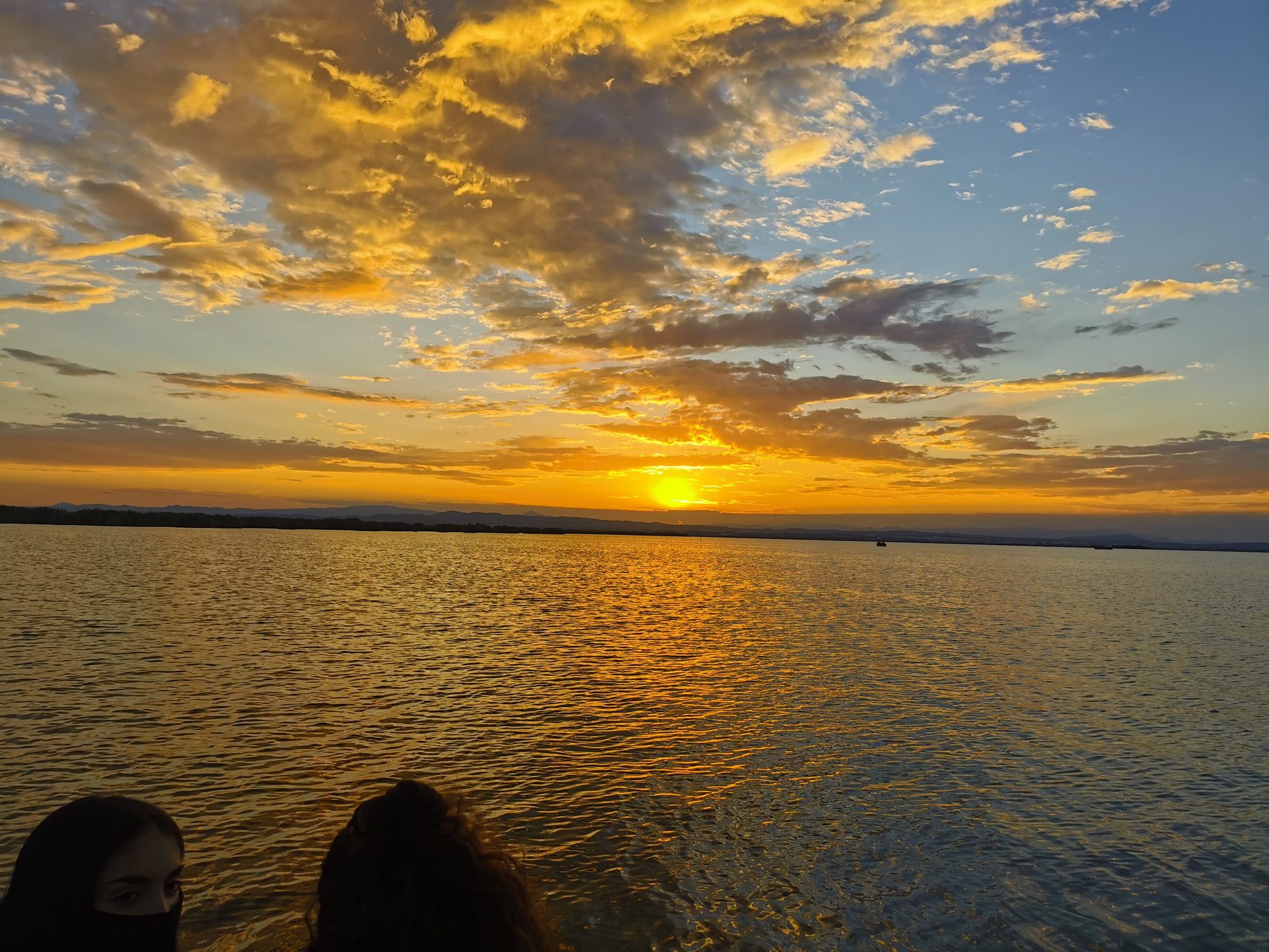 Puesta de sol dorada sobre el agua con nubes iluminadas en el horizonte.