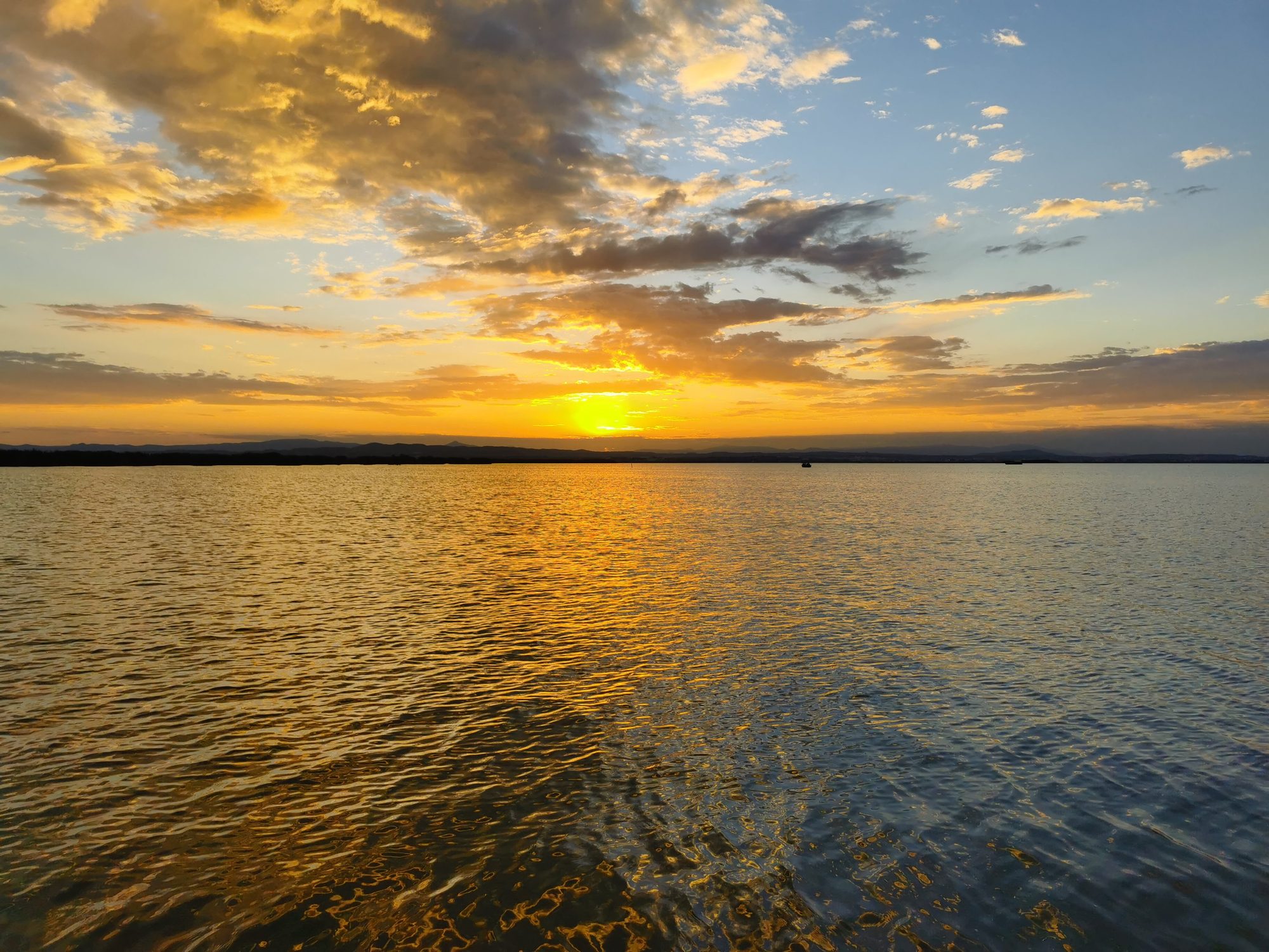 Puesta de sol dorada reflejándose sobre las aguas tranquilas de una laguna con nubes dispersas.