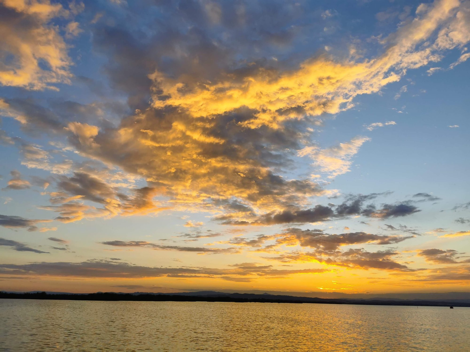 Atardecer dorado con nubes iluminadas sobre las aguas tranquilas de la albufera.