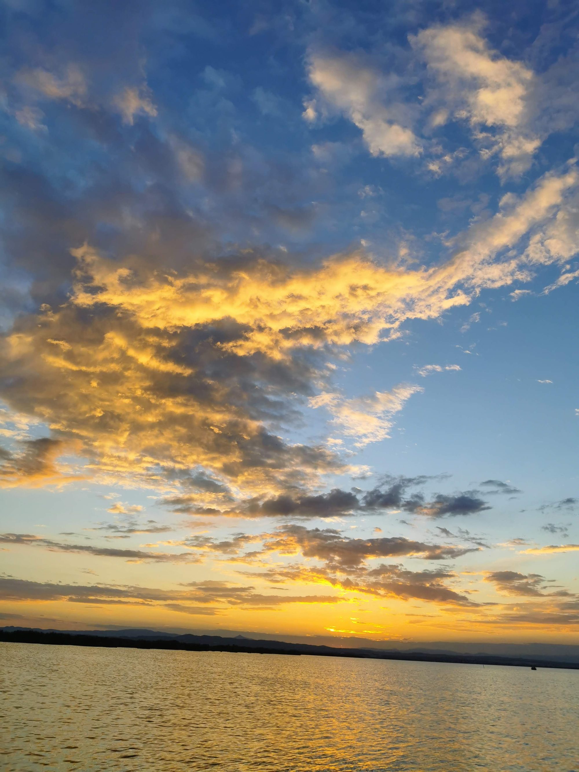 Atardecer dorado con nubes sobre el agua tranquila frente al horizonte lejano.