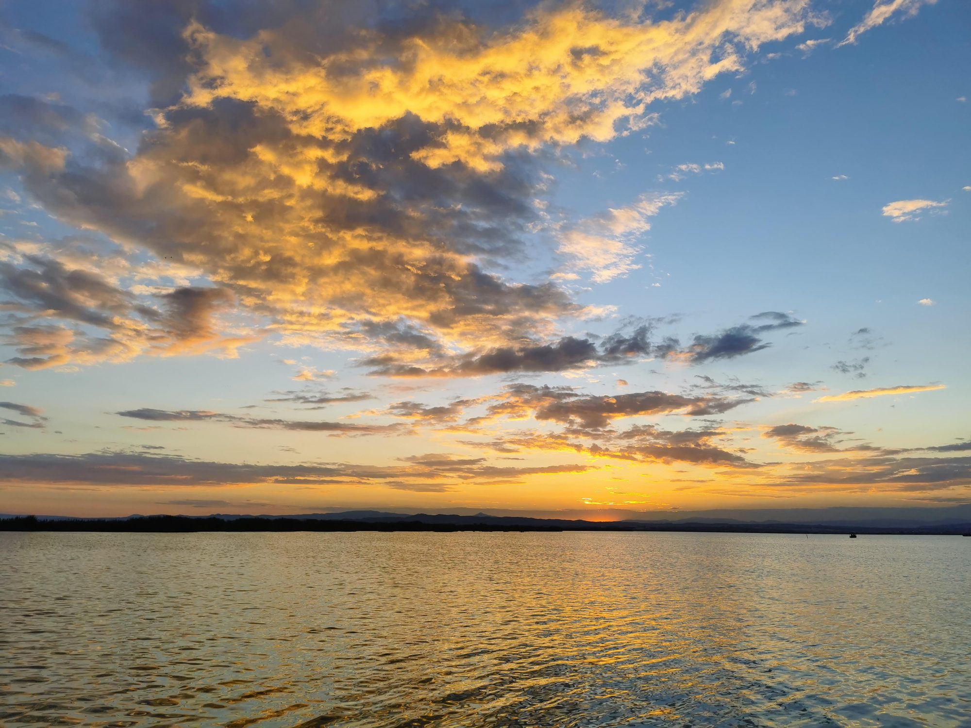 Atardecer dorado sobre aguas tranquilas con nubes iluminadas por el sol poniente.
