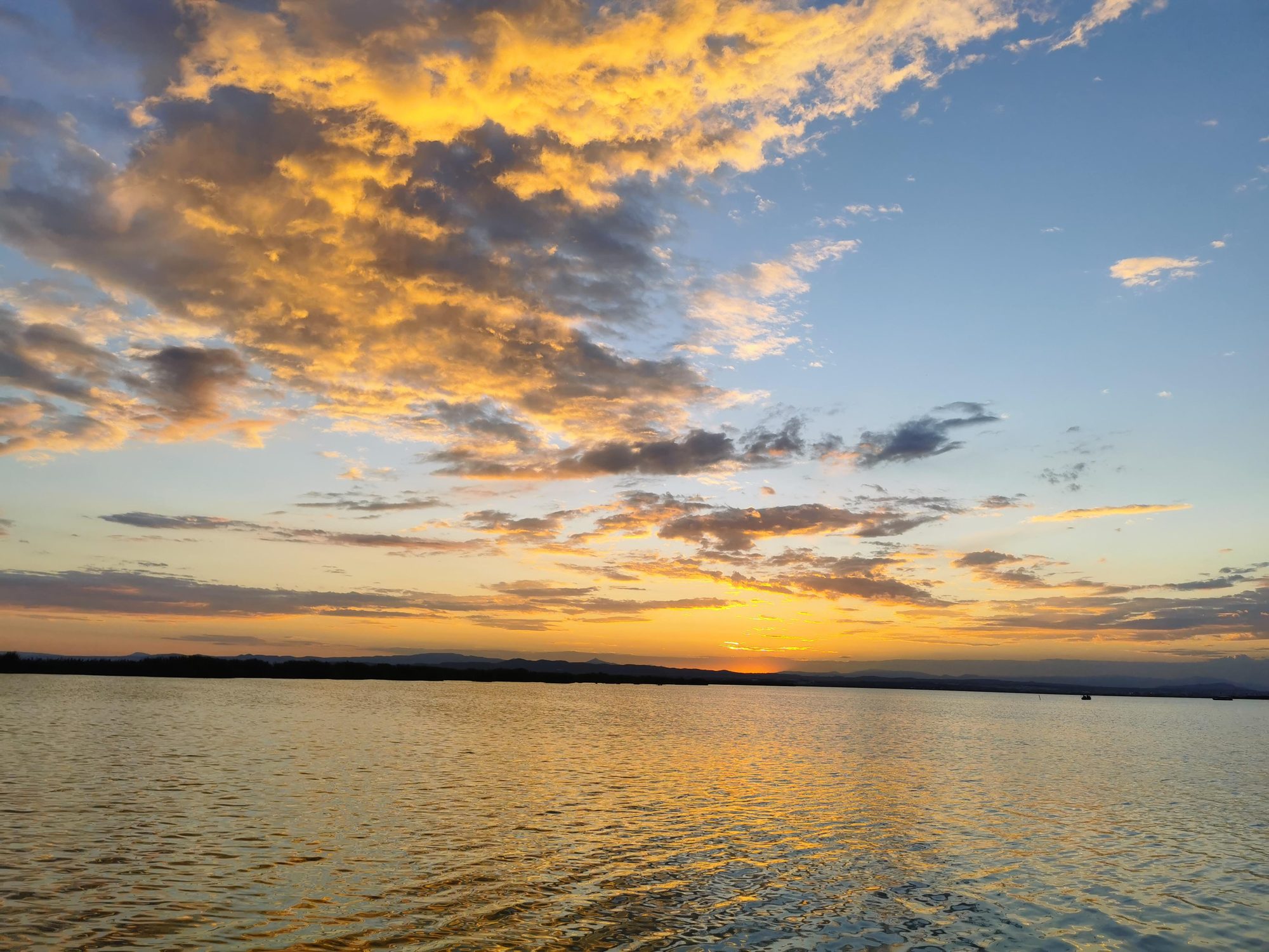 Puesta de sol con nubes doradas sobre el agua tranquila en Valencia.