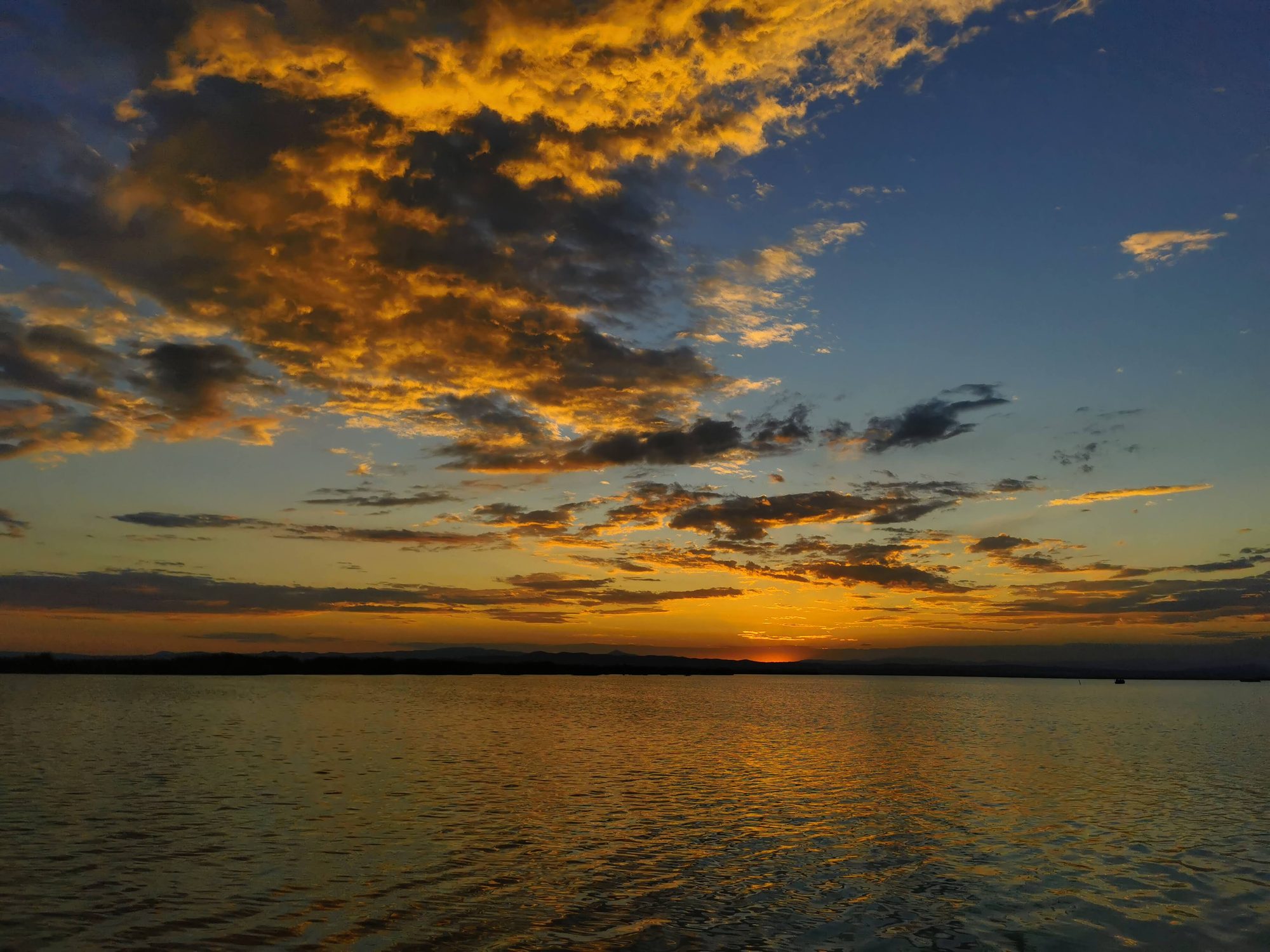 Atardecer dorado sobre aguas tranquilas con nubes iluminadas por el sol poniente.