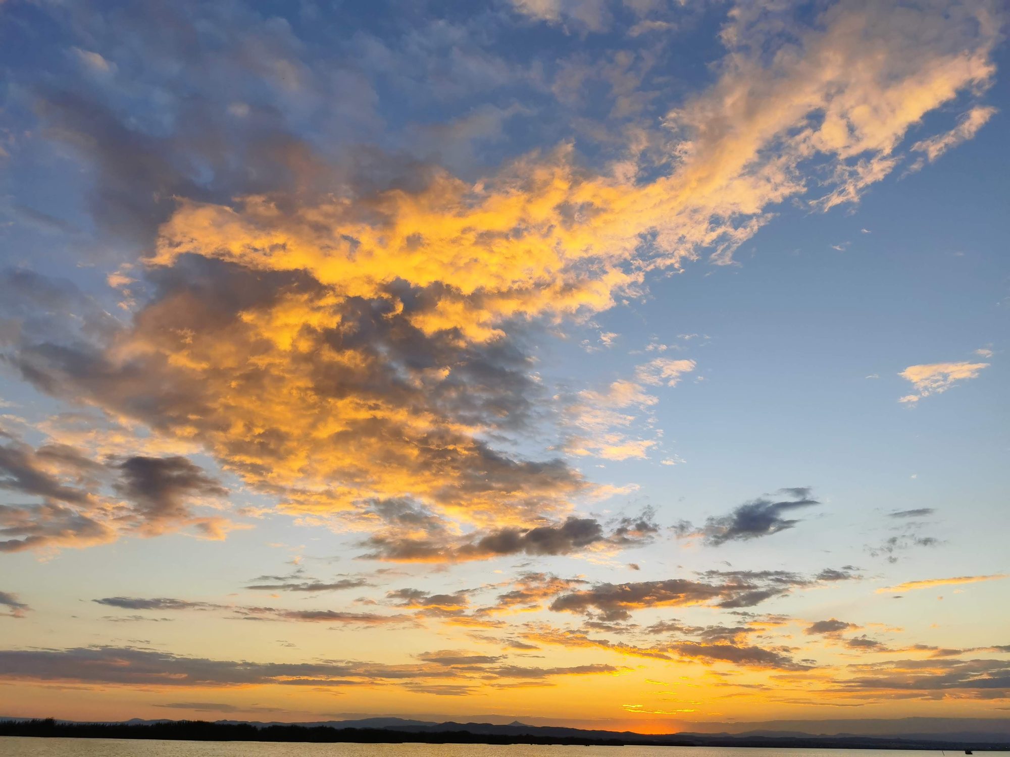 Atardecer dorado con nubes iluminadas sobre el horizonte de agua y montañas lejanas.
