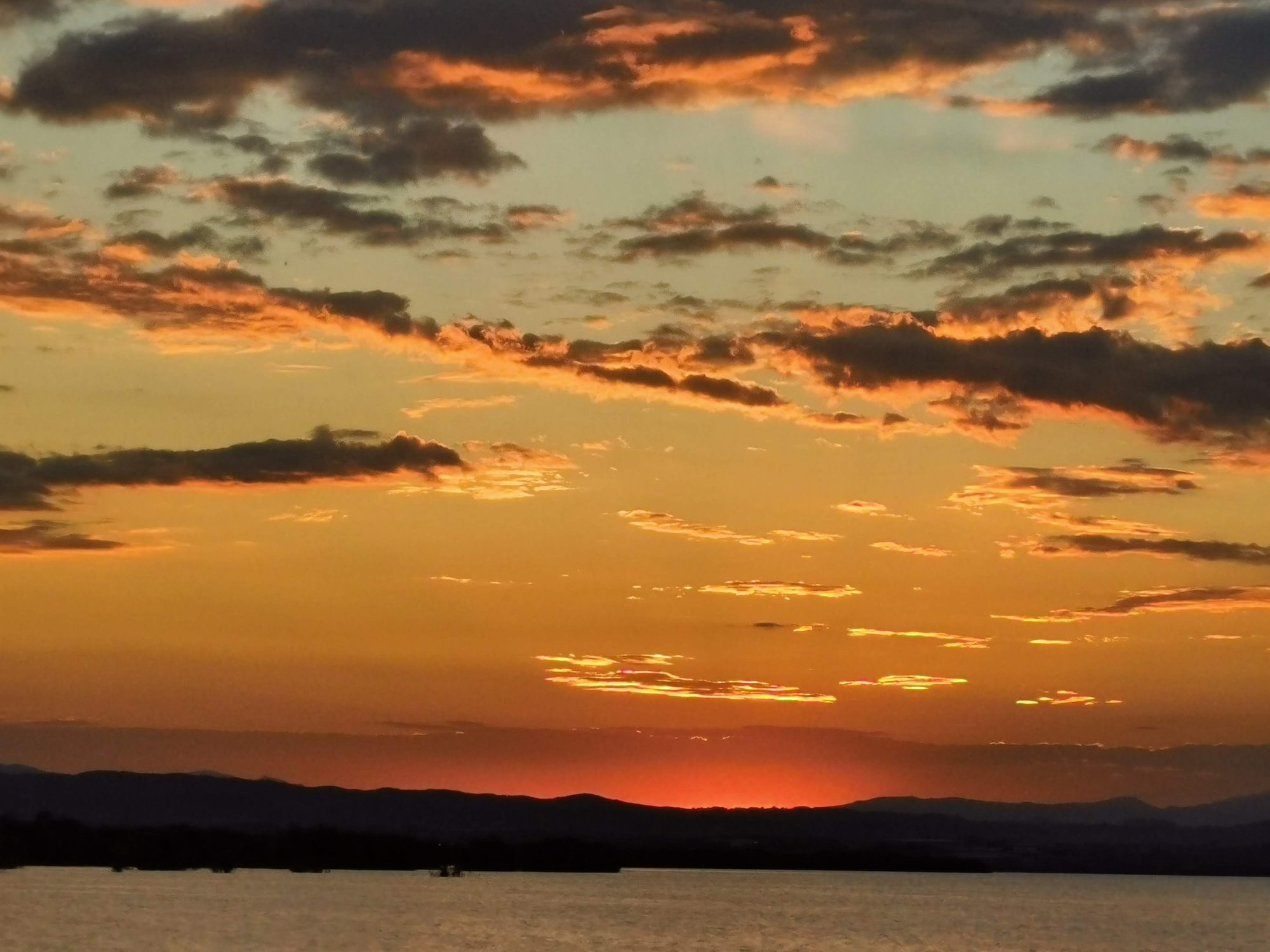 Atardecer naranja con nubes sobre el horizonte y agua en calma en Valencia.