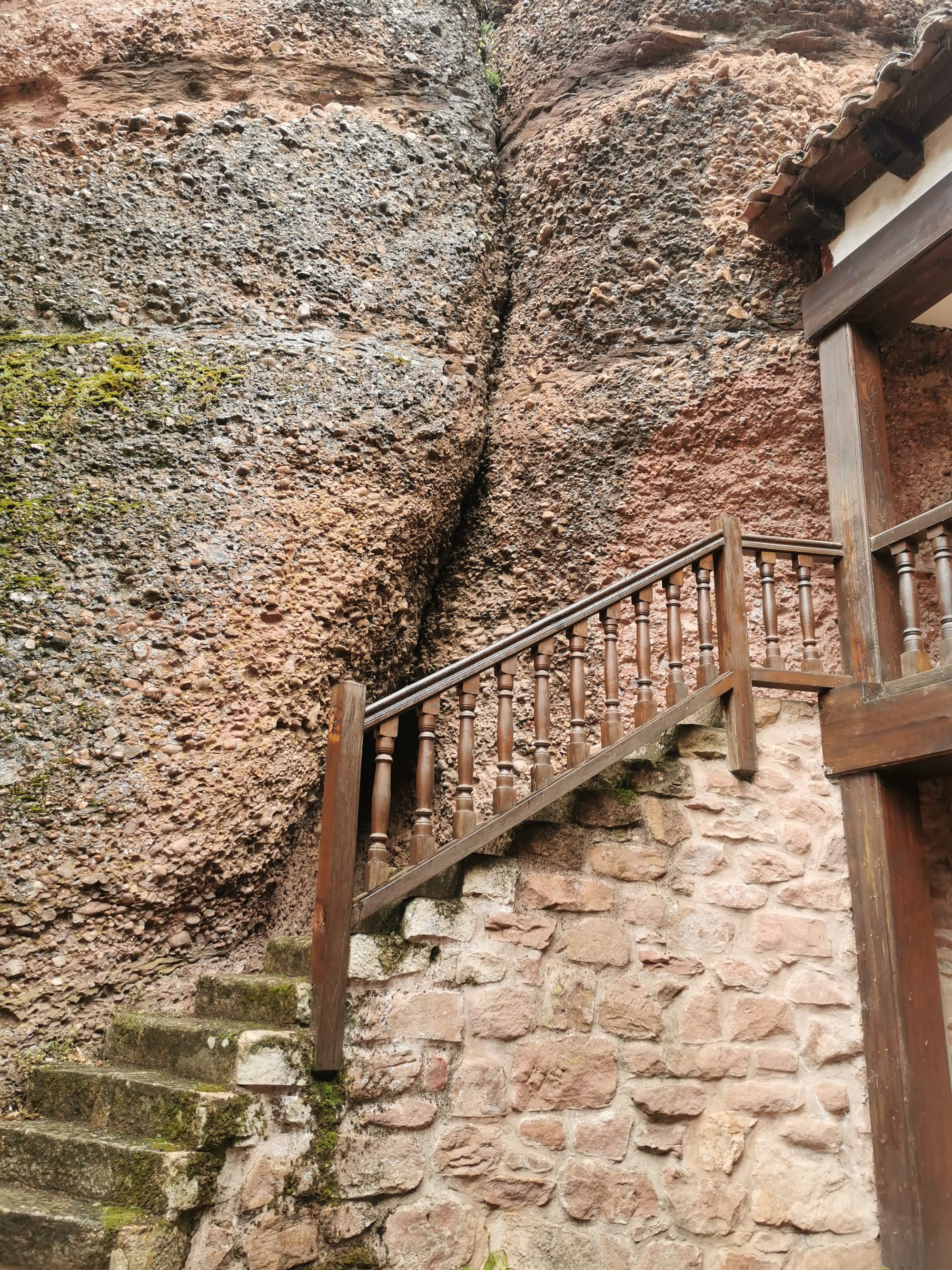 Escalera rústica de piedra y madera adosada a una gran pared rocosa vertical.