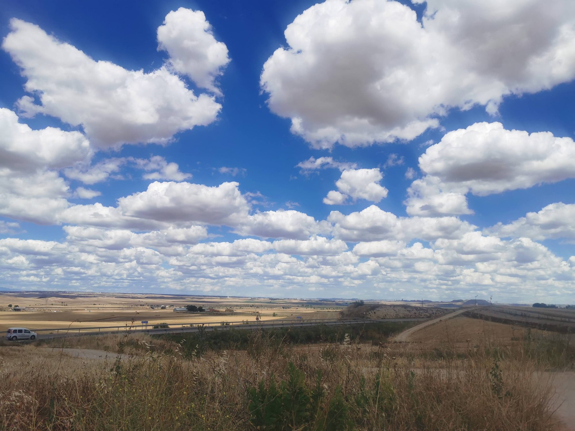 Paisaje castellano con campos secos bajo un inmenso cielo azul lleno de nubes blancas.