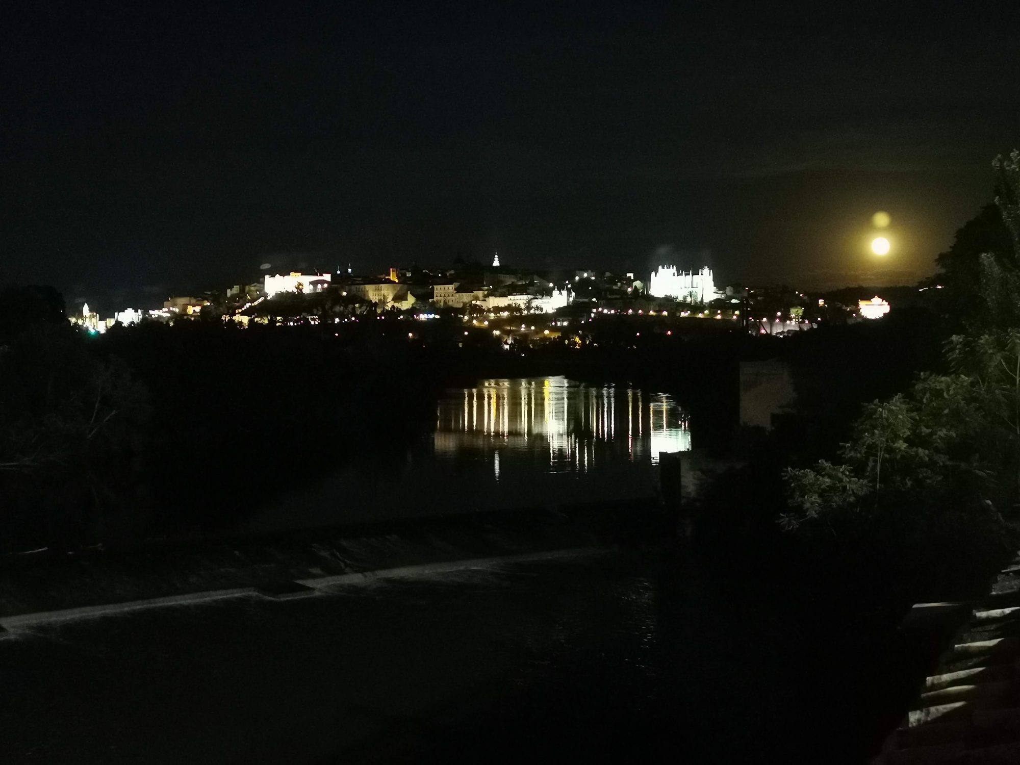 Vista nocturna de Toledo iluminada reflejada en el río Tajo bajo la luna.
