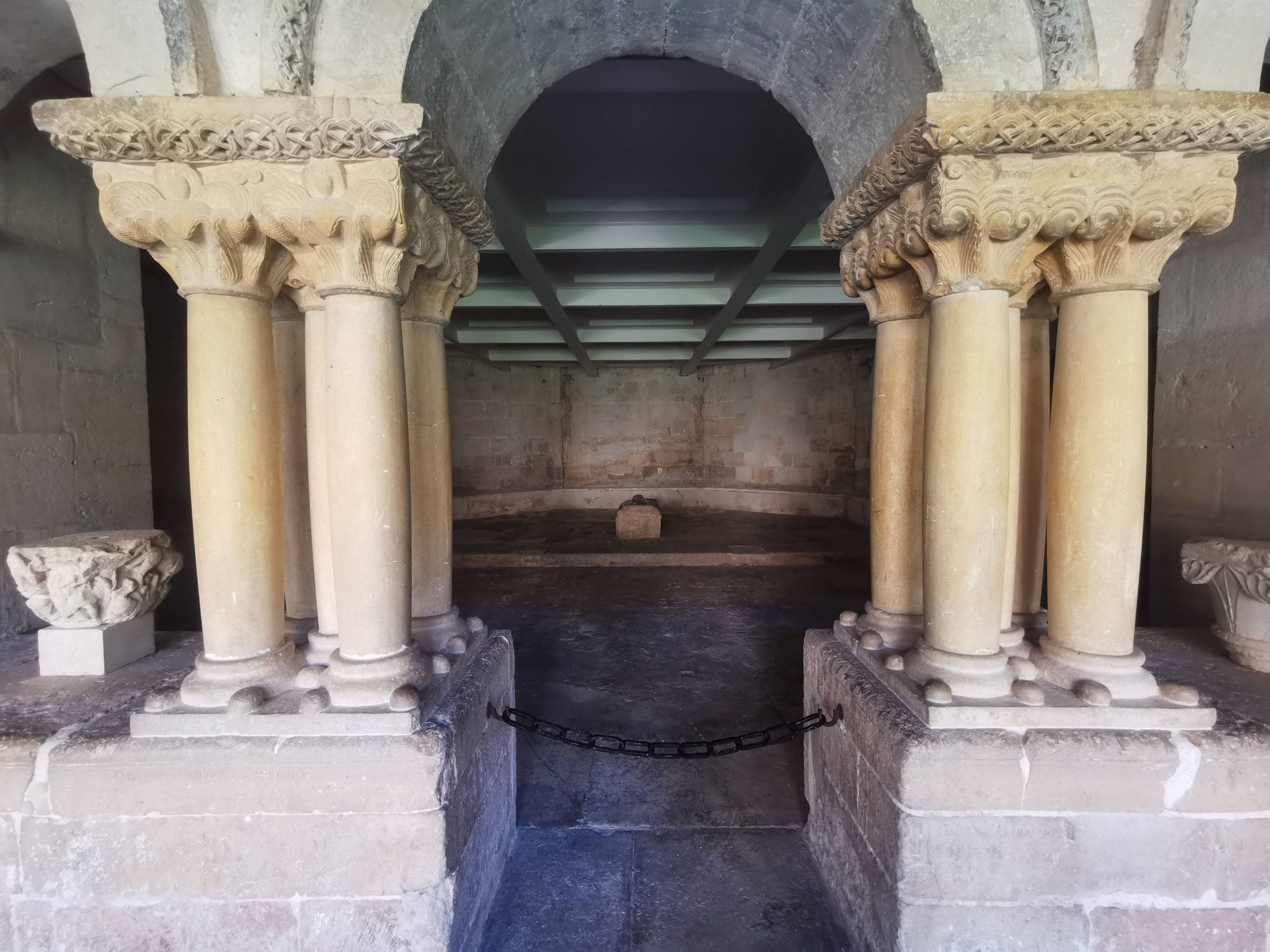 Arcos y columnas románicas de piedra con capiteles tallados en un recinto histórico.
