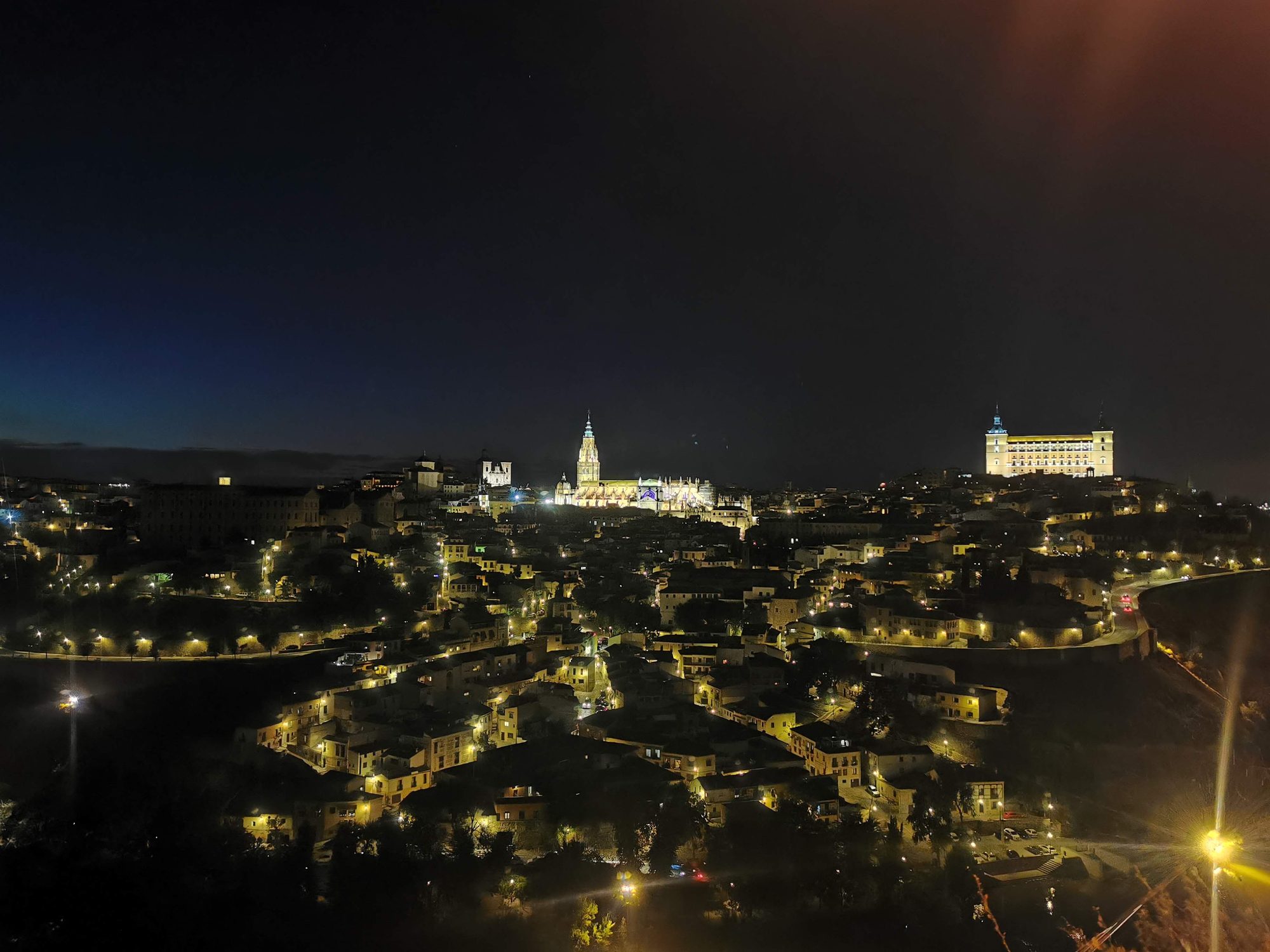Panorámica nocturna de Toledo iluminada con la catedral y el alcázar destacando en el horizonte.