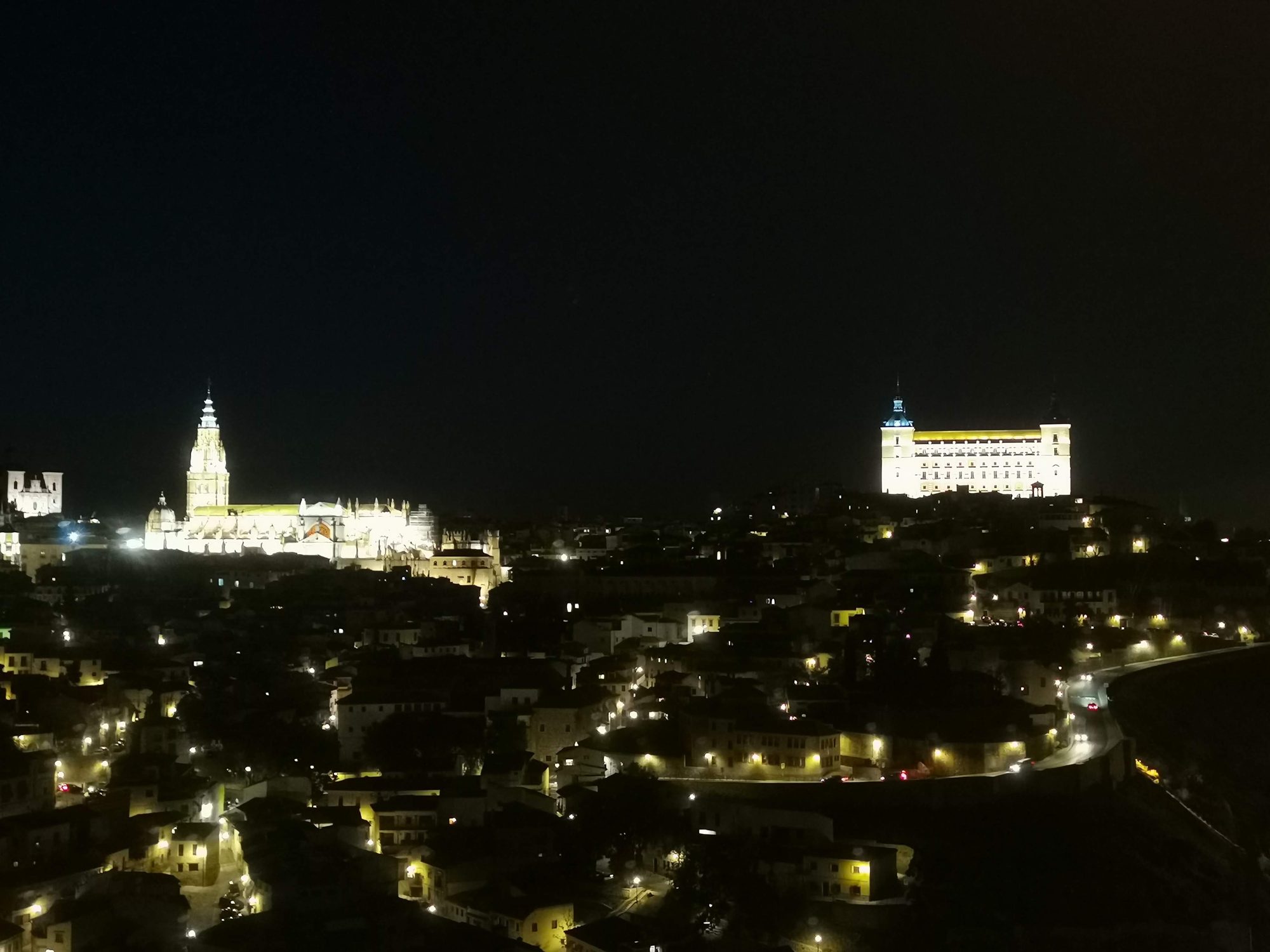Panorámica nocturna de Toledo con la catedral y el alcázar iluminados en la colina.