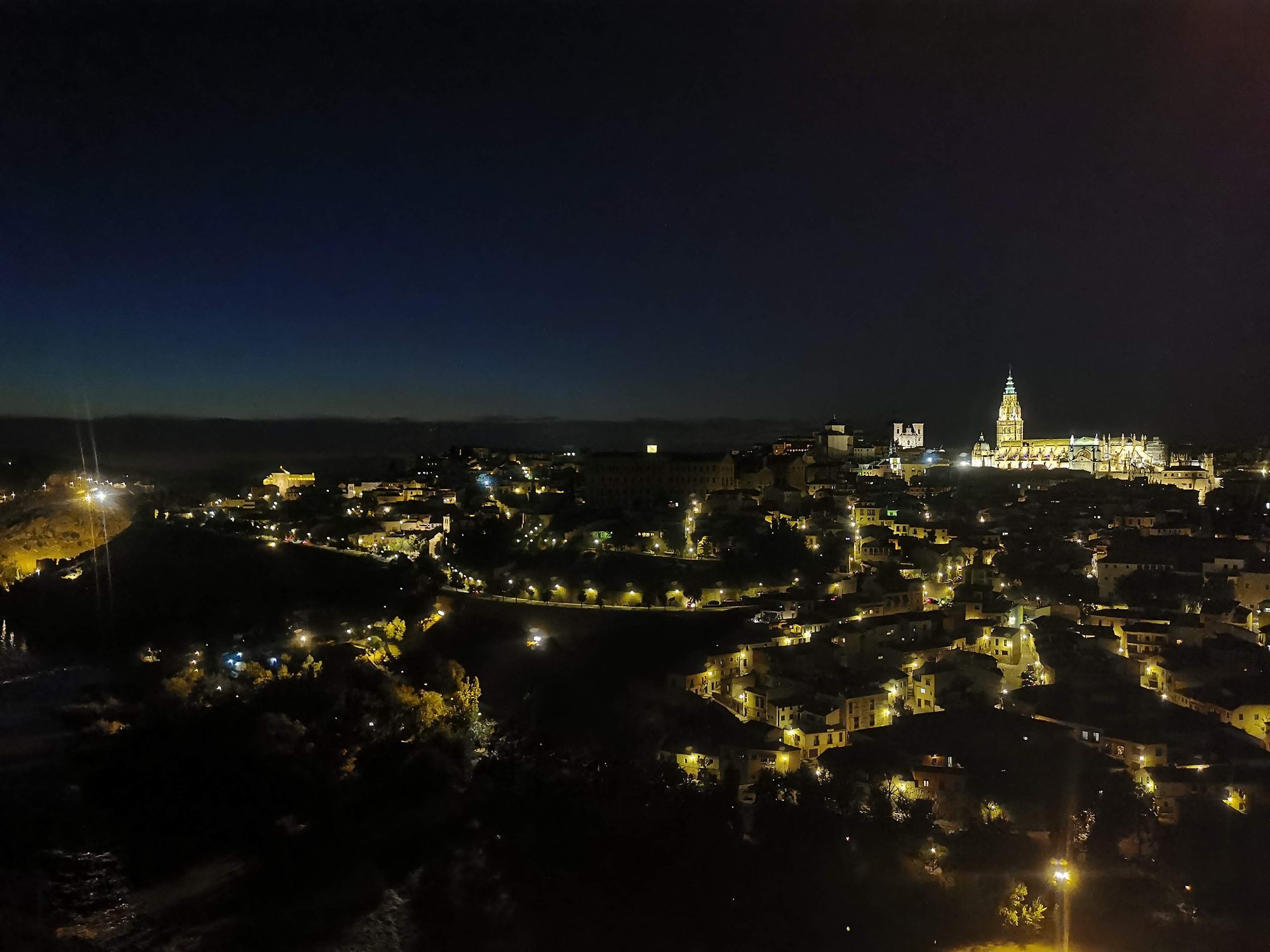 Panorámica nocturna de Toledo iluminada destacando la torre de la catedral en la colina.