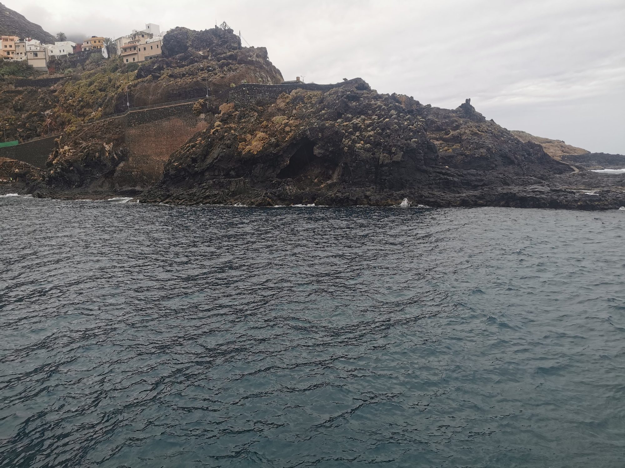 Acantilados volcánicos y casas junto al mar agitado bajo un cielo nublado.