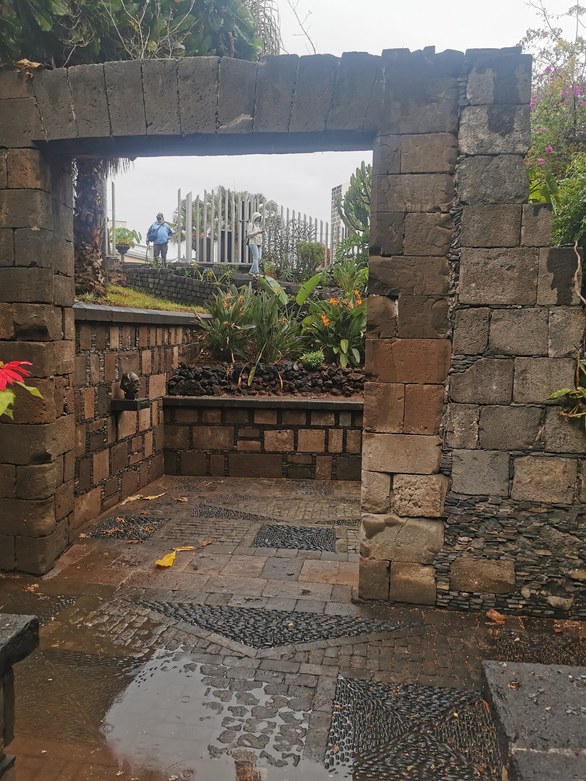 Arco de piedra volcánica y patio empedrado con vegetación tras la lluvia en Garachico.