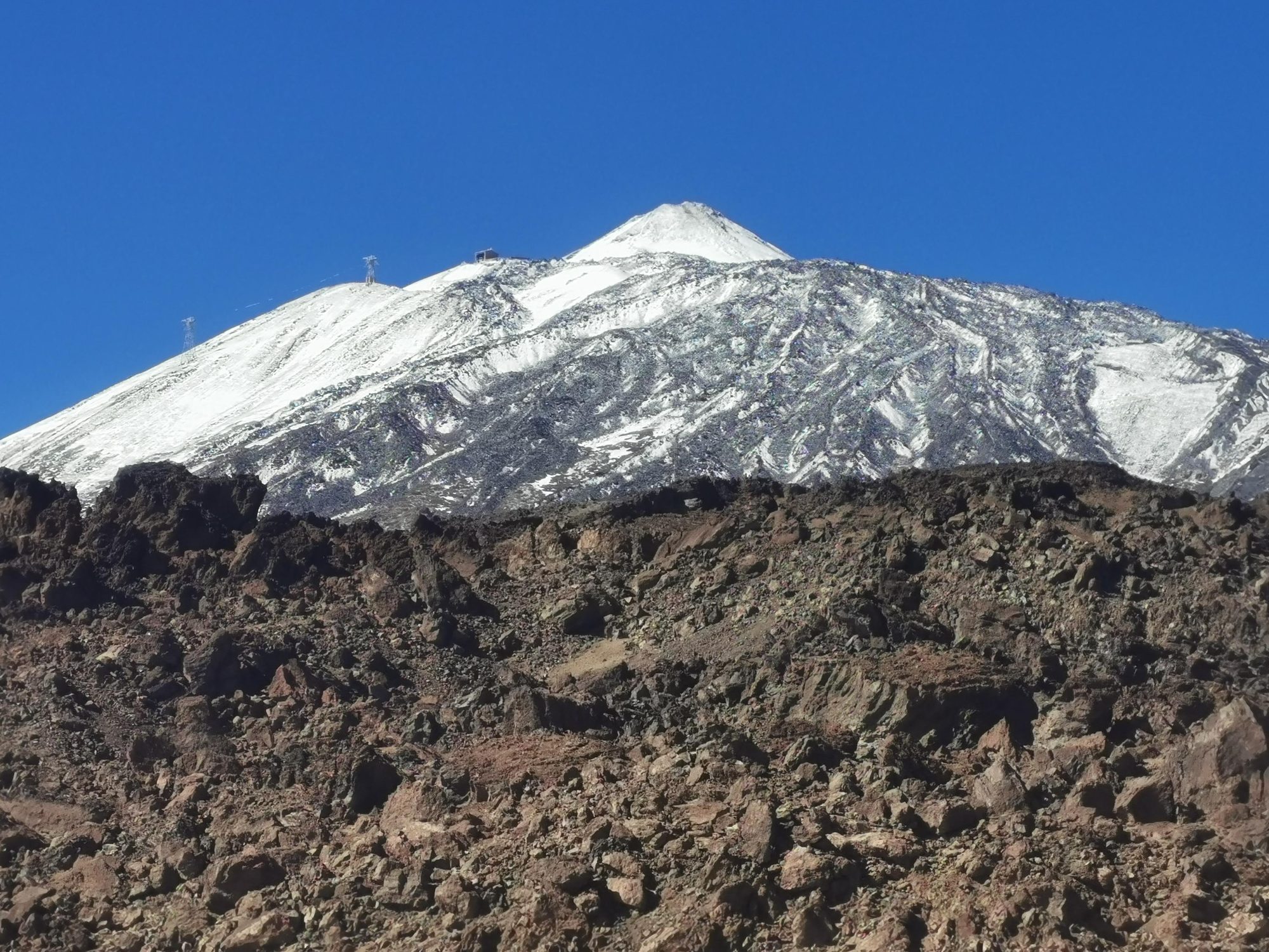Cima nevada del volcán Teide sobre terreno rocoso volcánico y cielo azul despejado.