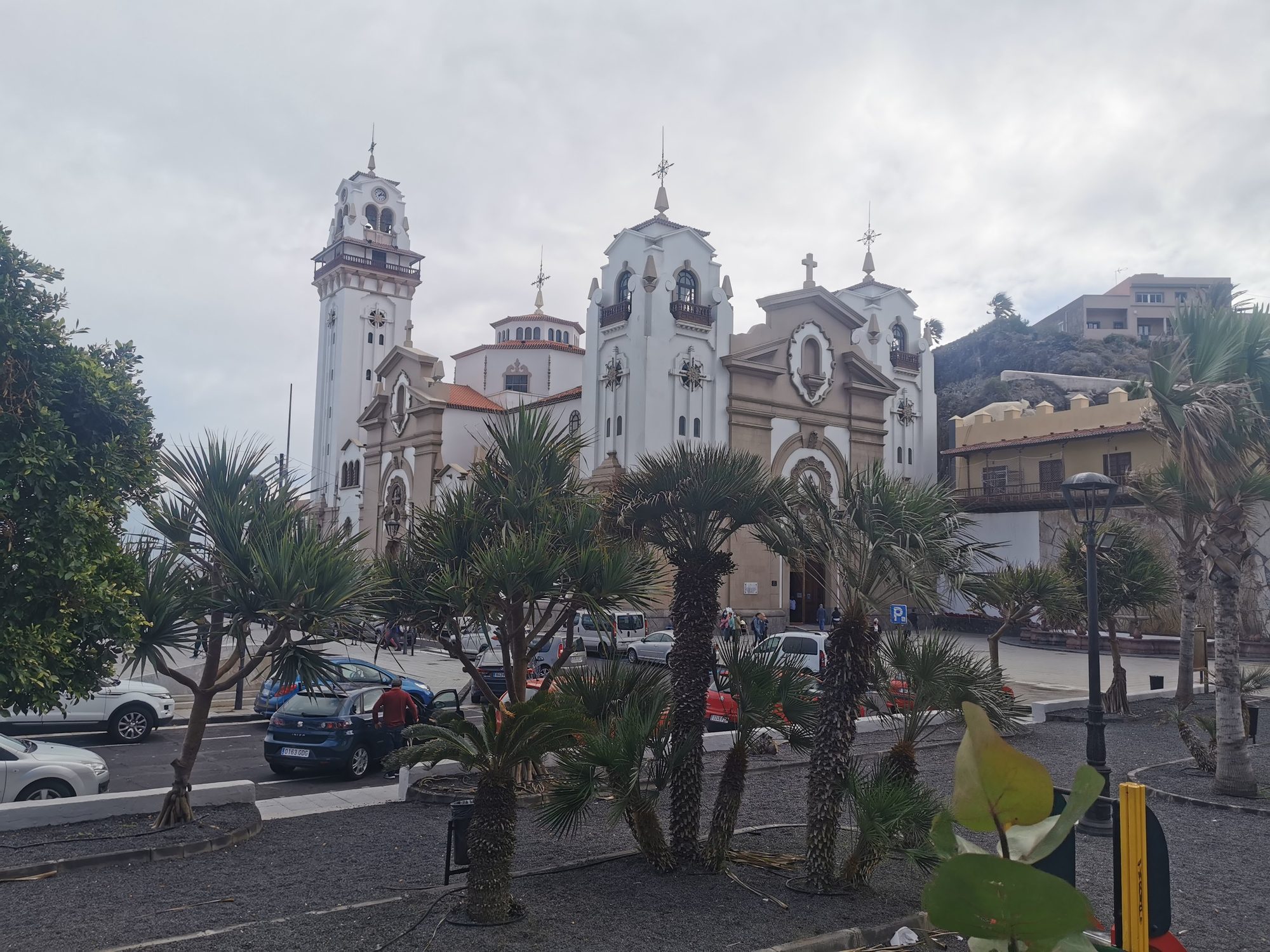 Basílica de Nuestra Señora de la Candelaria rodeada de palmeras bajo cielo nublado.