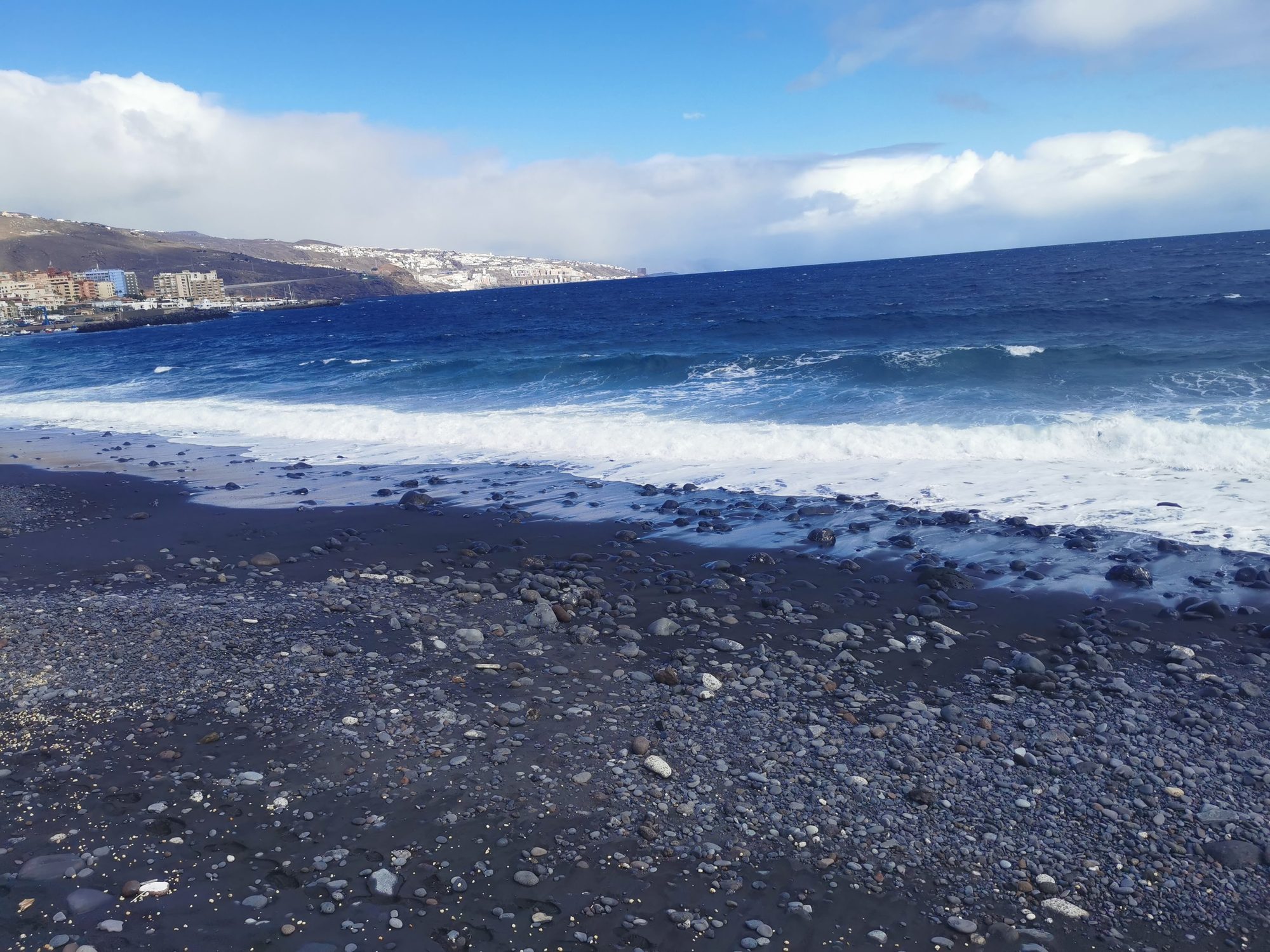 Playa de arena negra y piedras volcánicas con olas del mar en la costa.