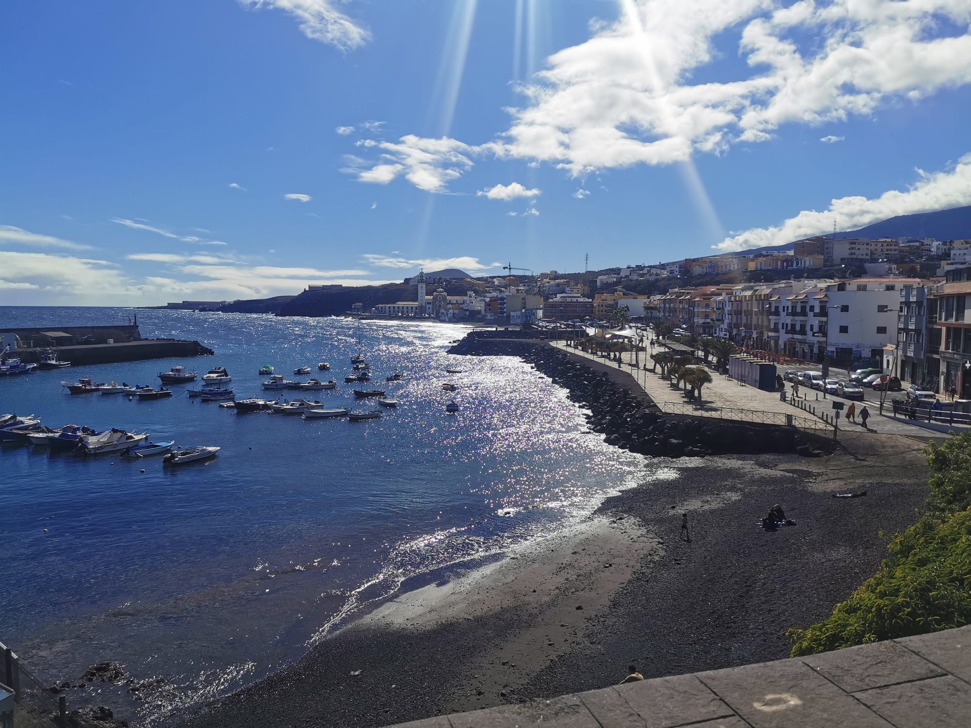 Puerto costero y playa de arena negra con barcos bajo el sol en Candelaria.