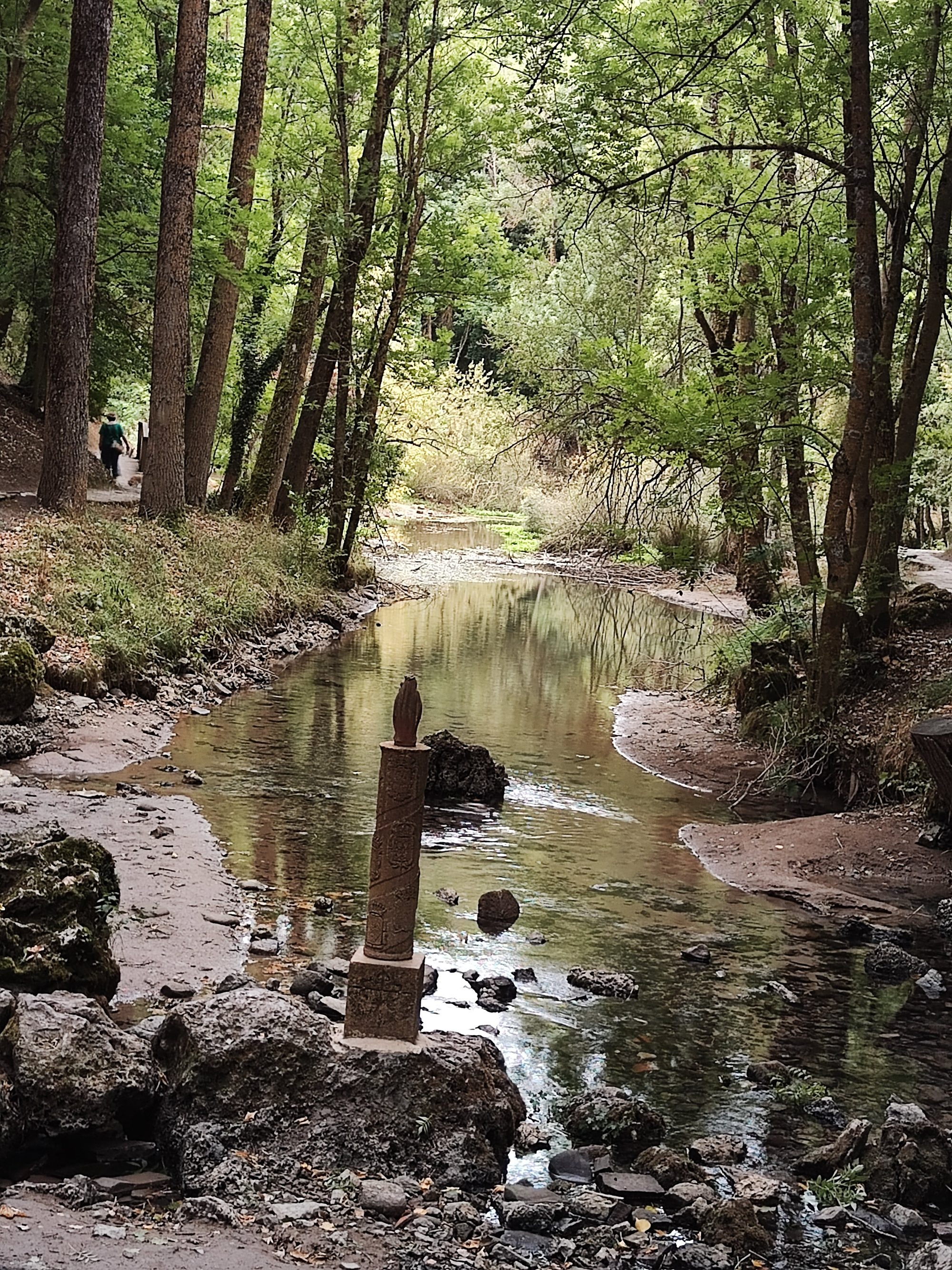Río sereno rodeado de un frondoso bosque con una escultura de piedra en el agua