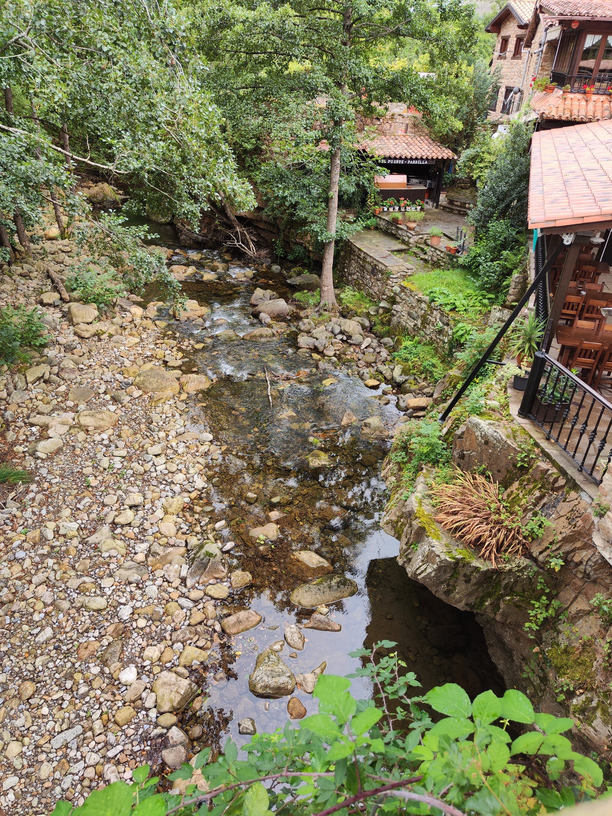 Río pedregoso de aguas claras junto a terrazas de piedra y frondosos árboles.