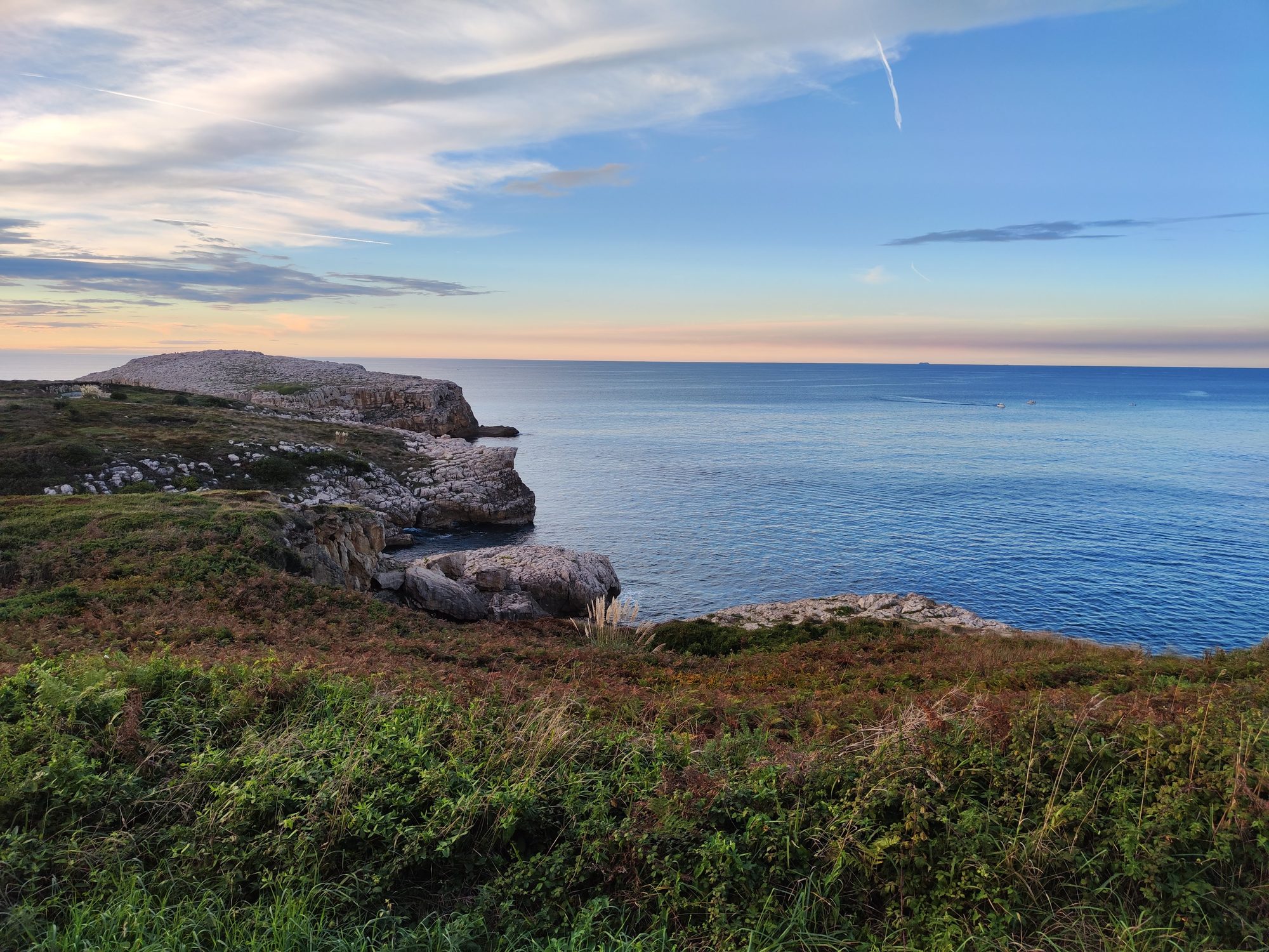Acantilados rocosos y costa verde frente al mar Cantábrico durante el atardecer.