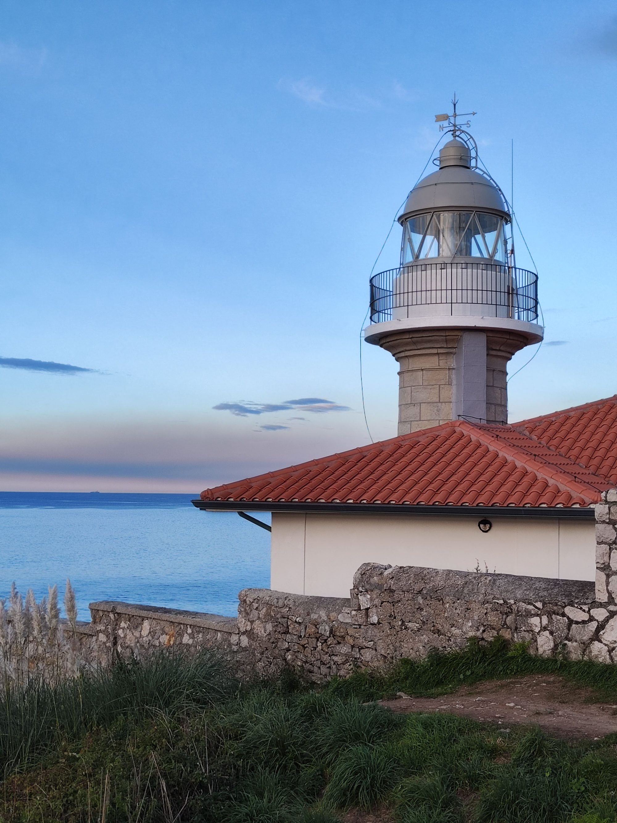 Faro de piedra con linterna acristalada y tejado rojo junto al mar en Suances.