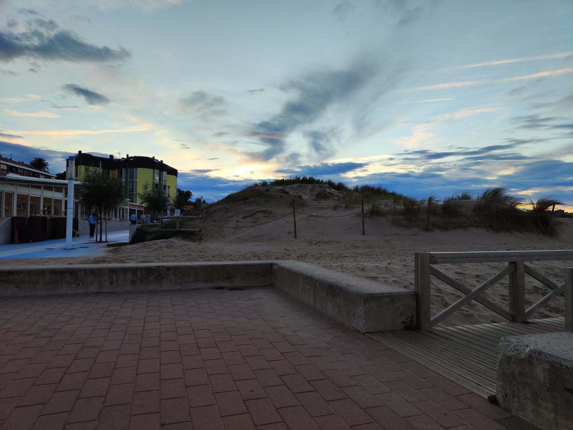 Paseo marítimo de adoquines junto a dunas de arena bajo un cielo al atardecer.