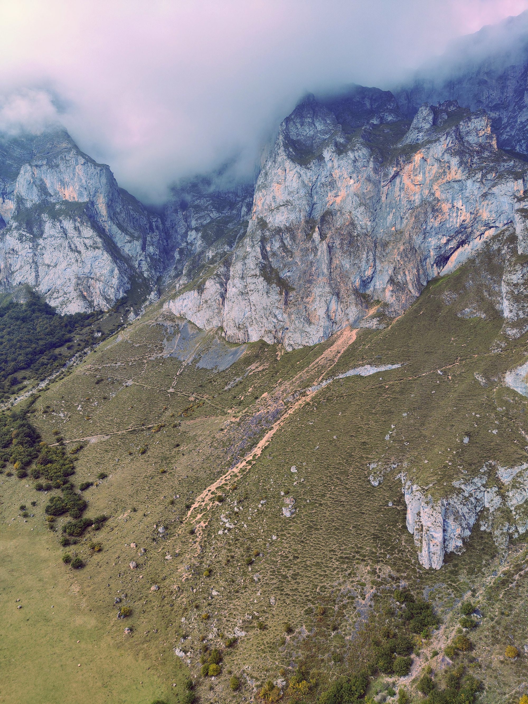 Imponentes montañas rocosas de los Picos de Europa envueltas en niebla y laderas verdes.