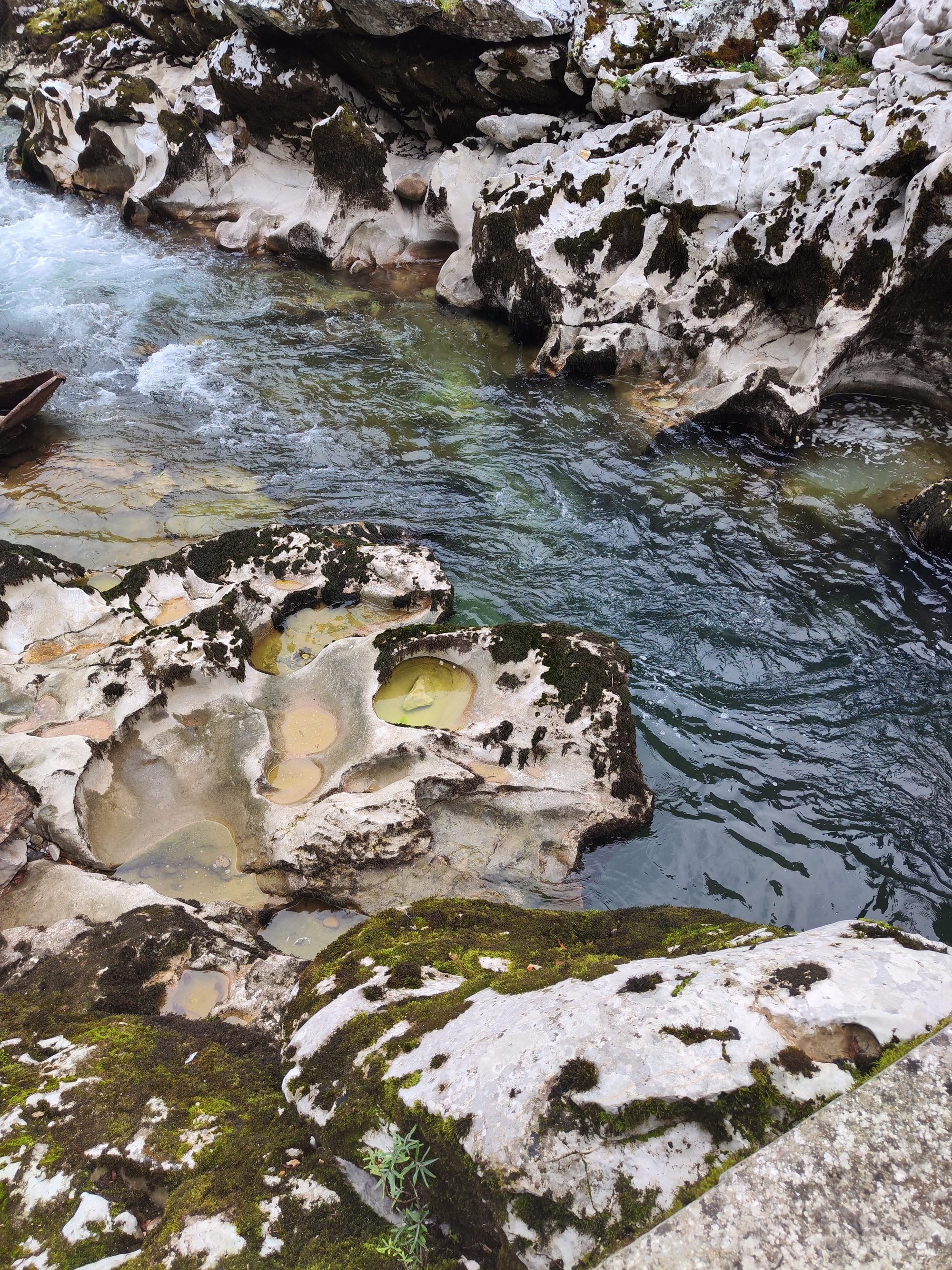 Río de aguas cristalinas fluyendo entre rocas calizas erosionadas con pozas y musgo.