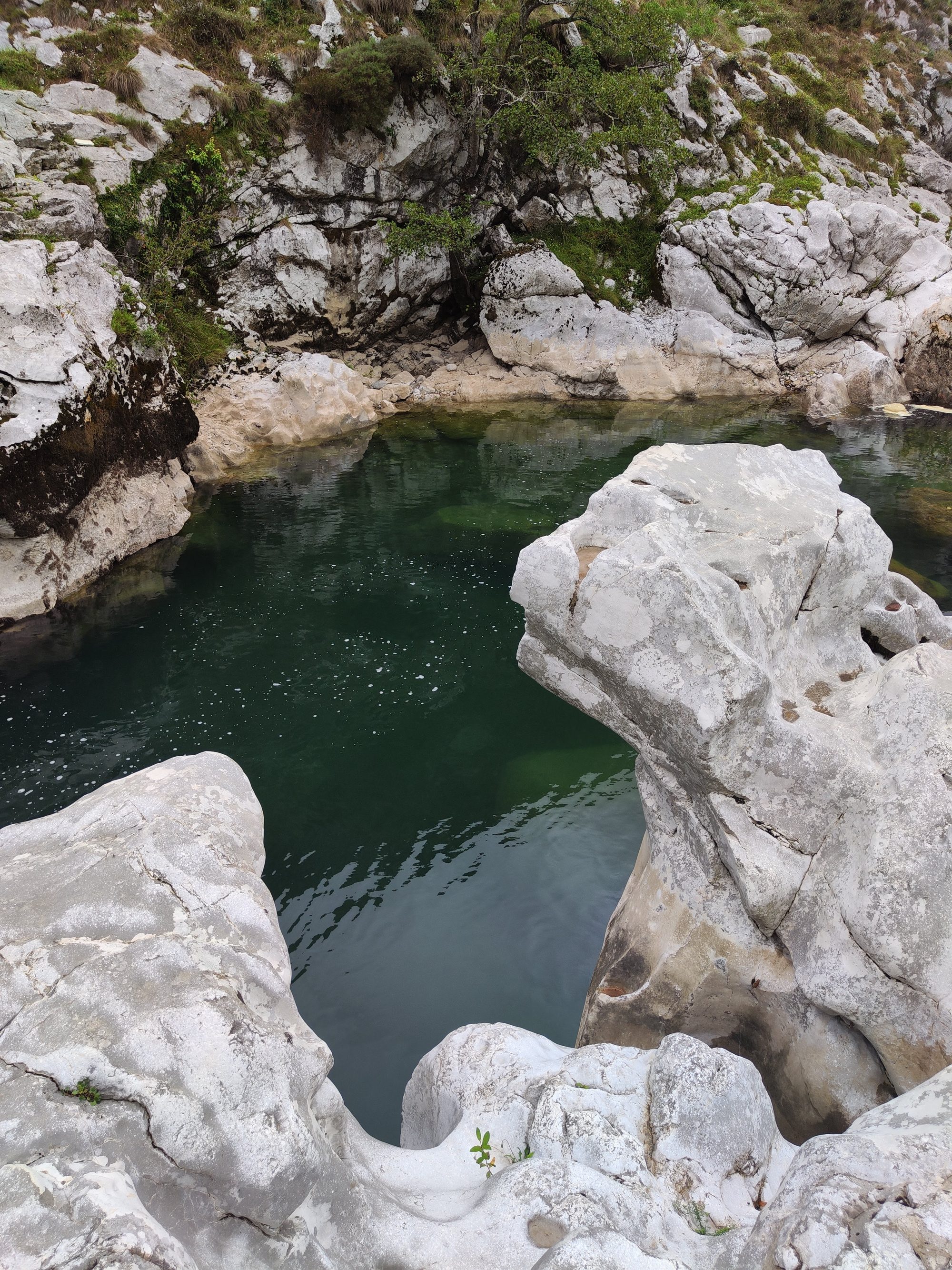 Poza natural de aguas verdes cristalinas rodeada de grandes rocas calizas erosionadas en la montaña.