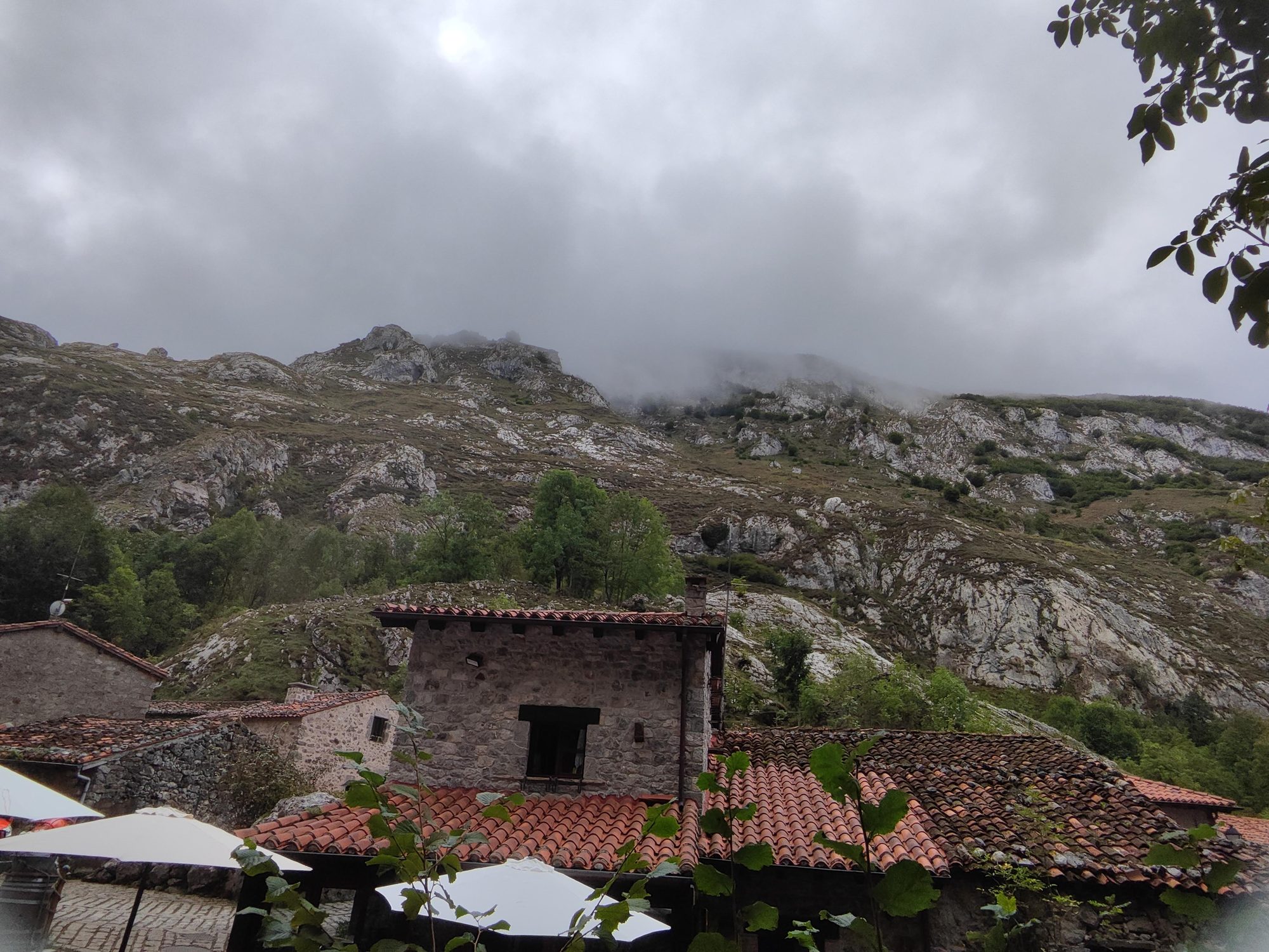 Casas de piedra tradicionales bajo imponentes montañas rocosas cubiertas de niebla en Cabrales.
